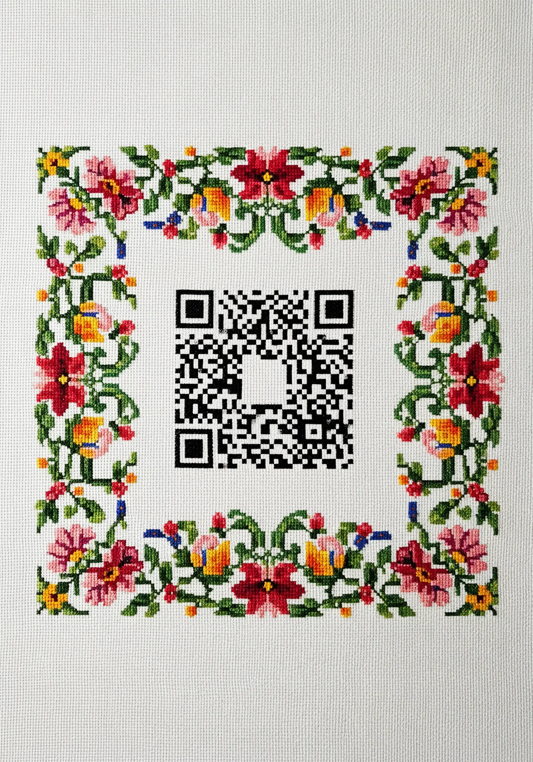 A cross-stitched QR code surrounded by a traditional, colorful floral border.