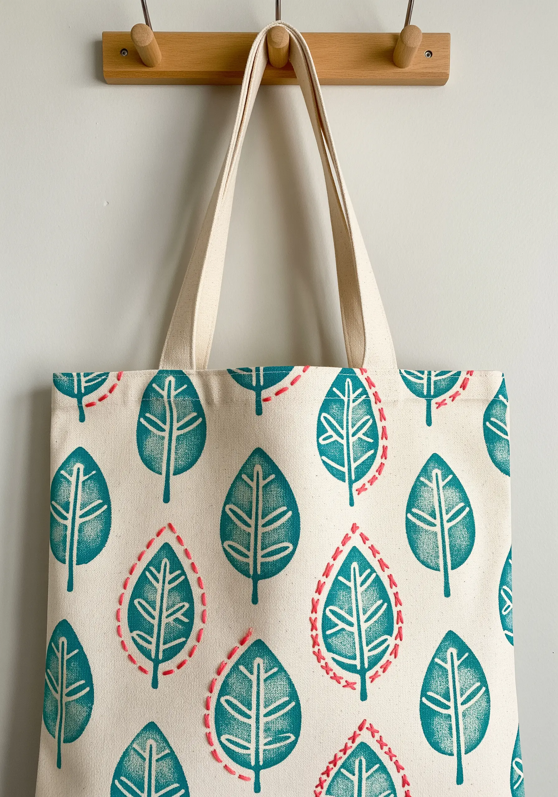 A canvas tote bag with a block-printed leaf pattern, with some leaves outlined in pink embroidery.