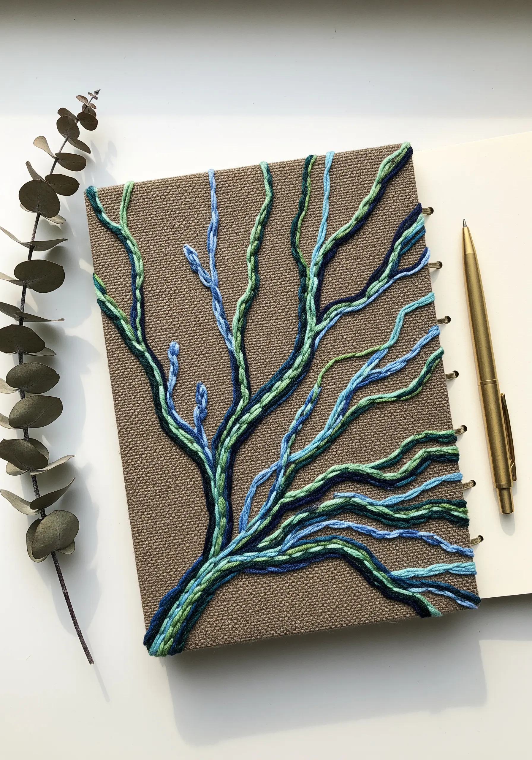 A journal cover decorated with raised chain stitches in blue and green, forming abstract branches.