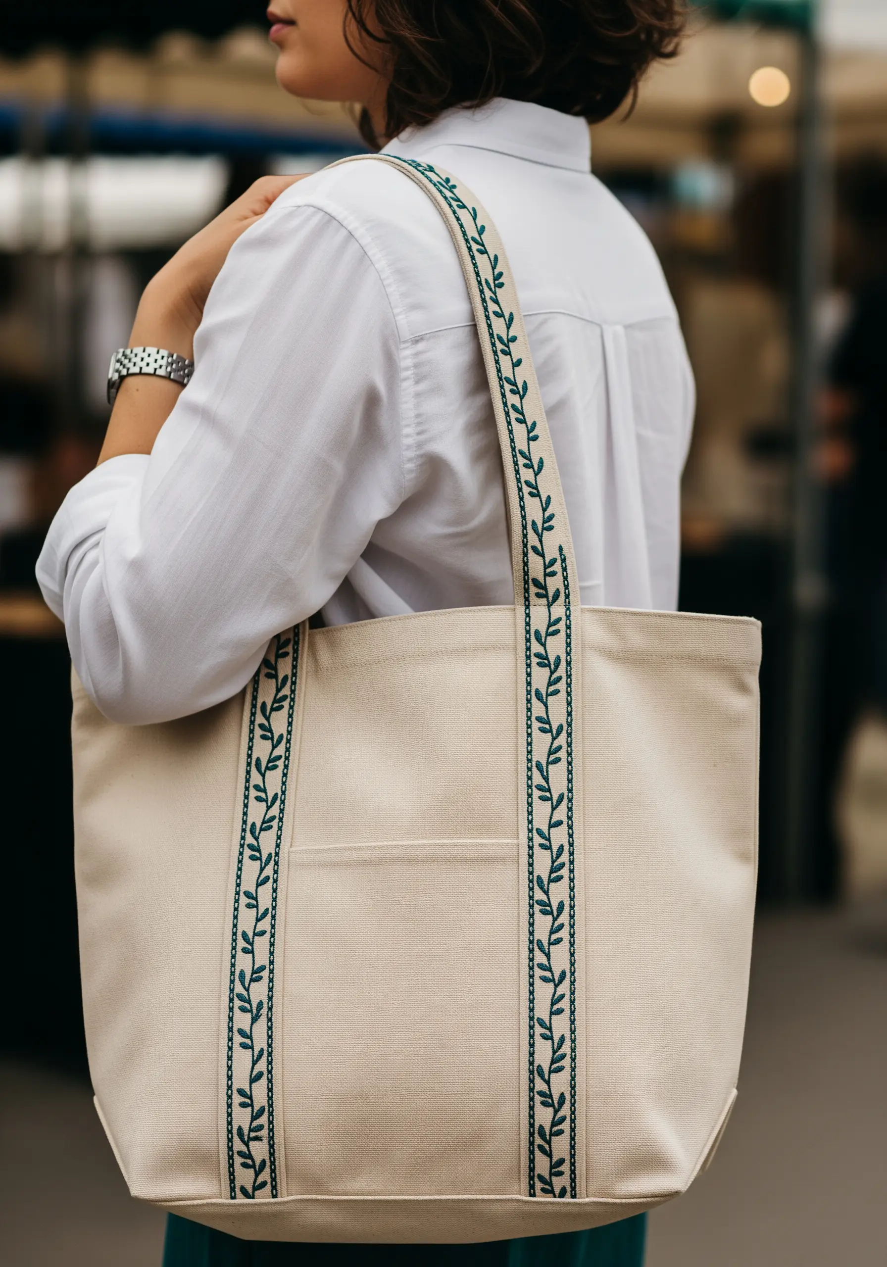 A repeating green leaf and vine pattern embroidered along the length of a tote bag's straps.