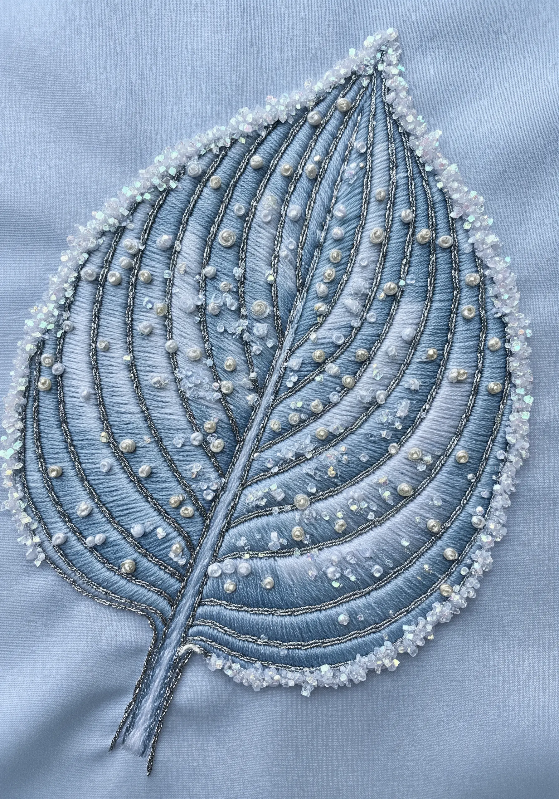 A blue embroidered leaf heavily embellished with white beads and iridescent sequins.