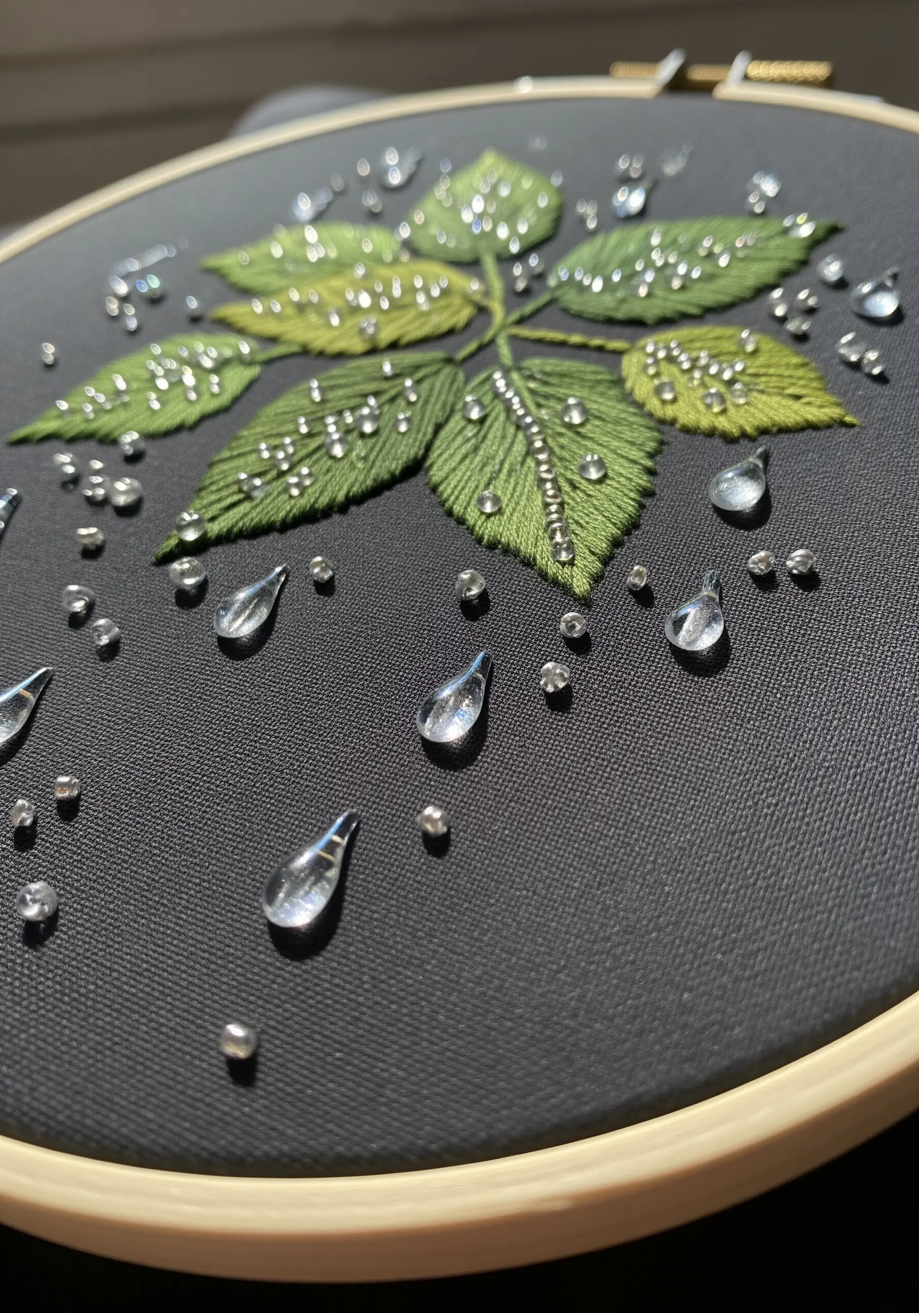 Green embroidered leaves on black fabric adorned with clear beads that look like raindrops.