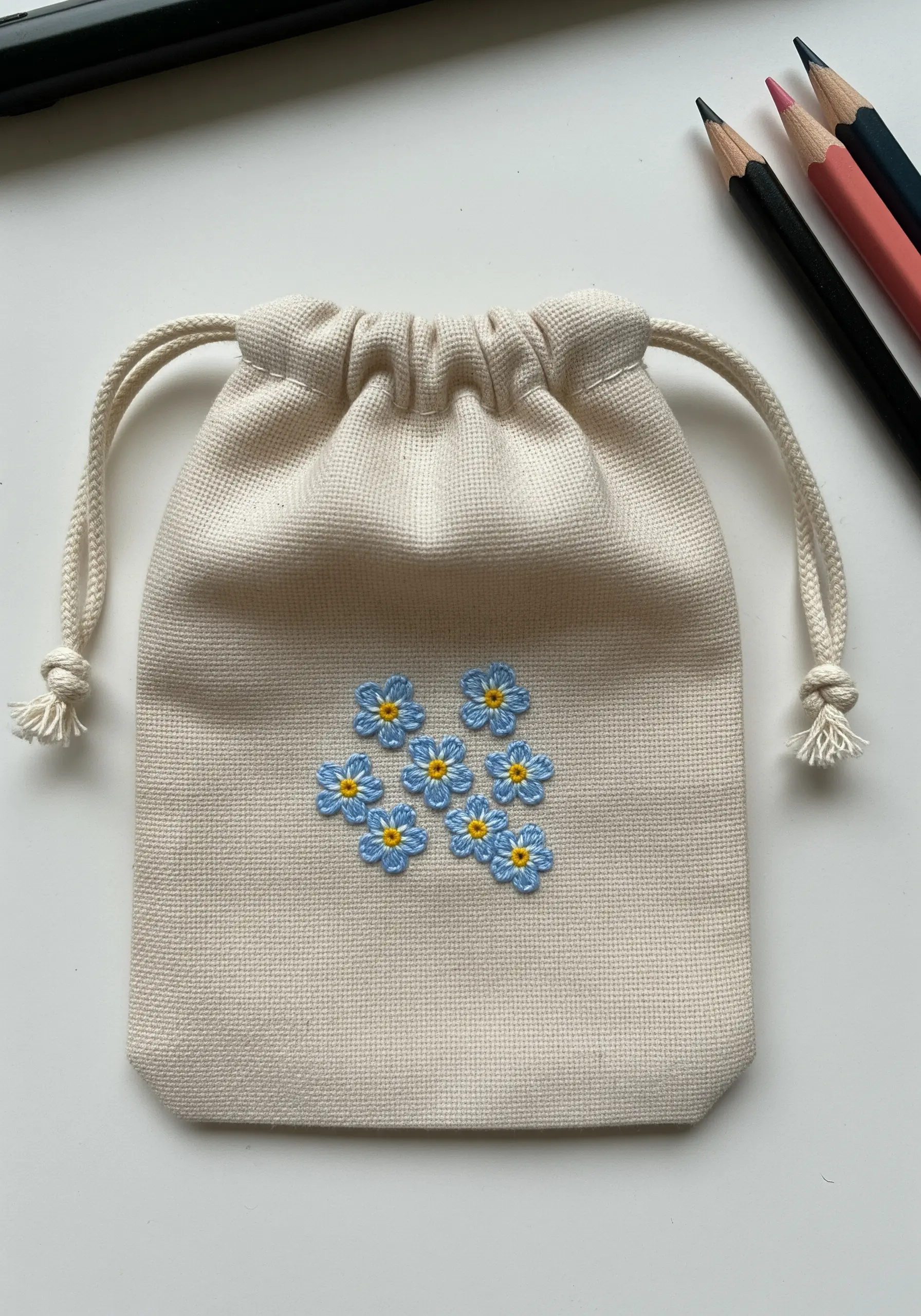 A small cluster of blue and yellow forget-me-not flowers on a canvas drawstring pouch.