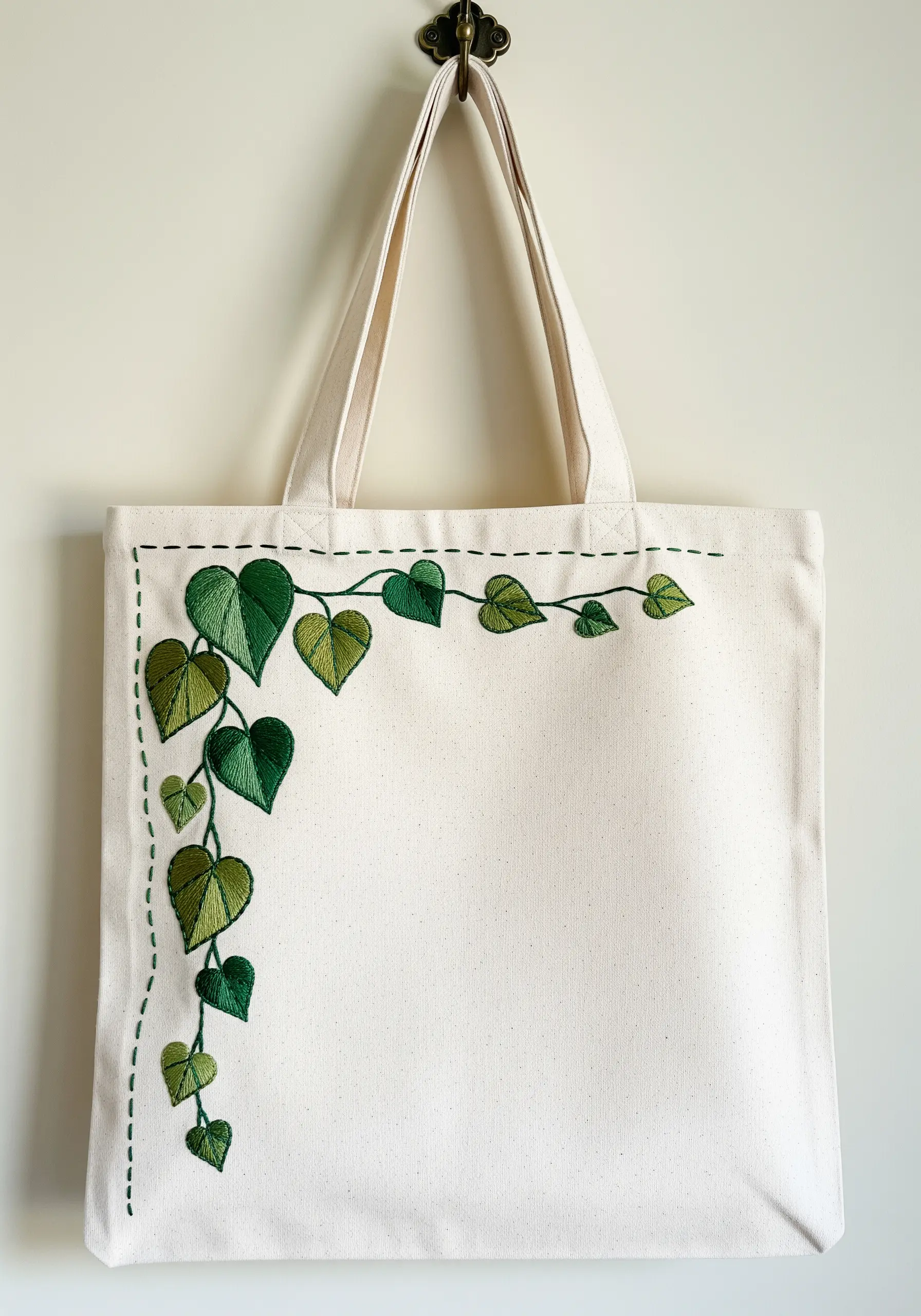 An ivy vine with gradient green leaves embroidered on the corner of a canvas tote bag.