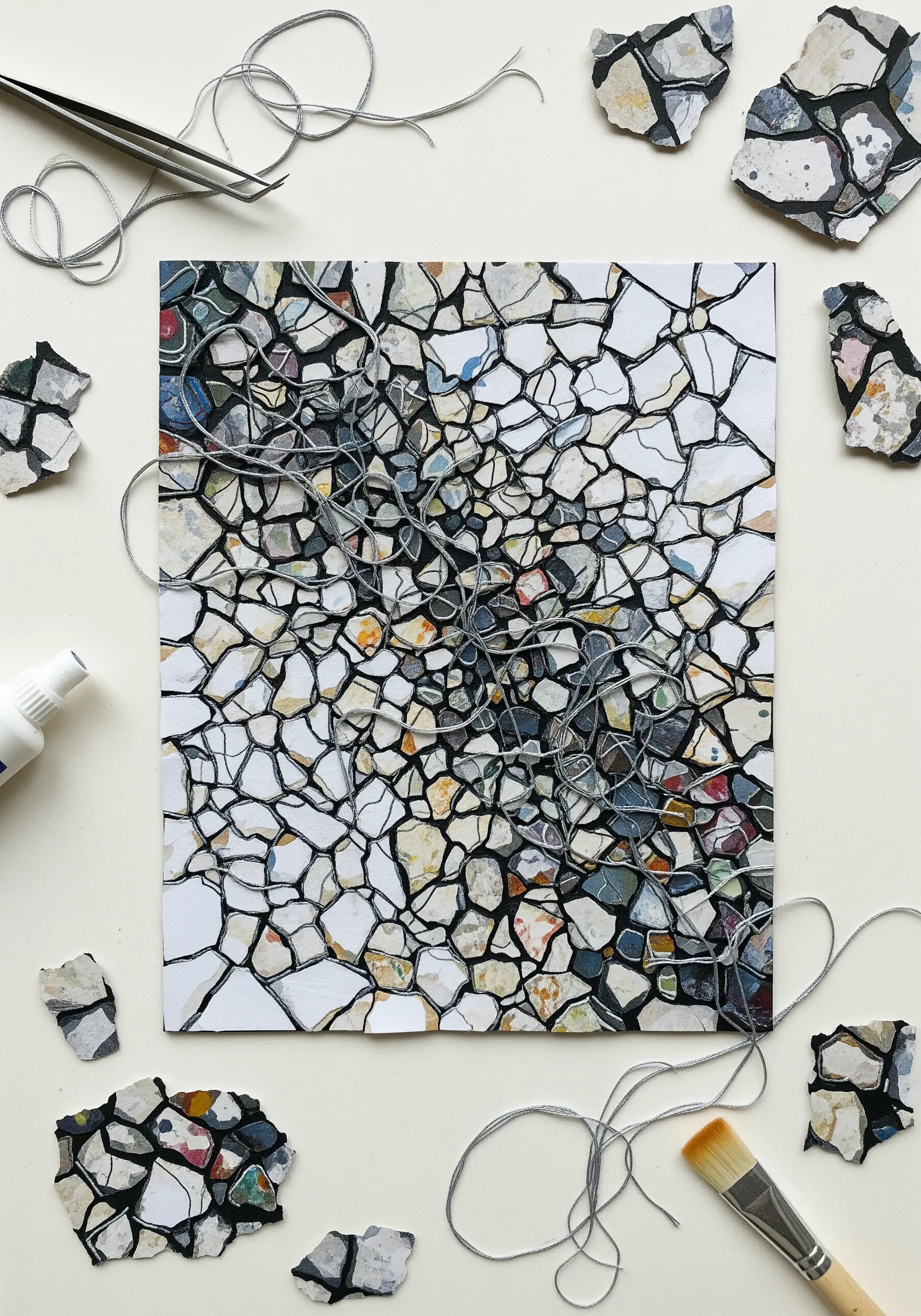 An abstract mosaic made from paper fragments with tangled grey thread visible between the pieces.