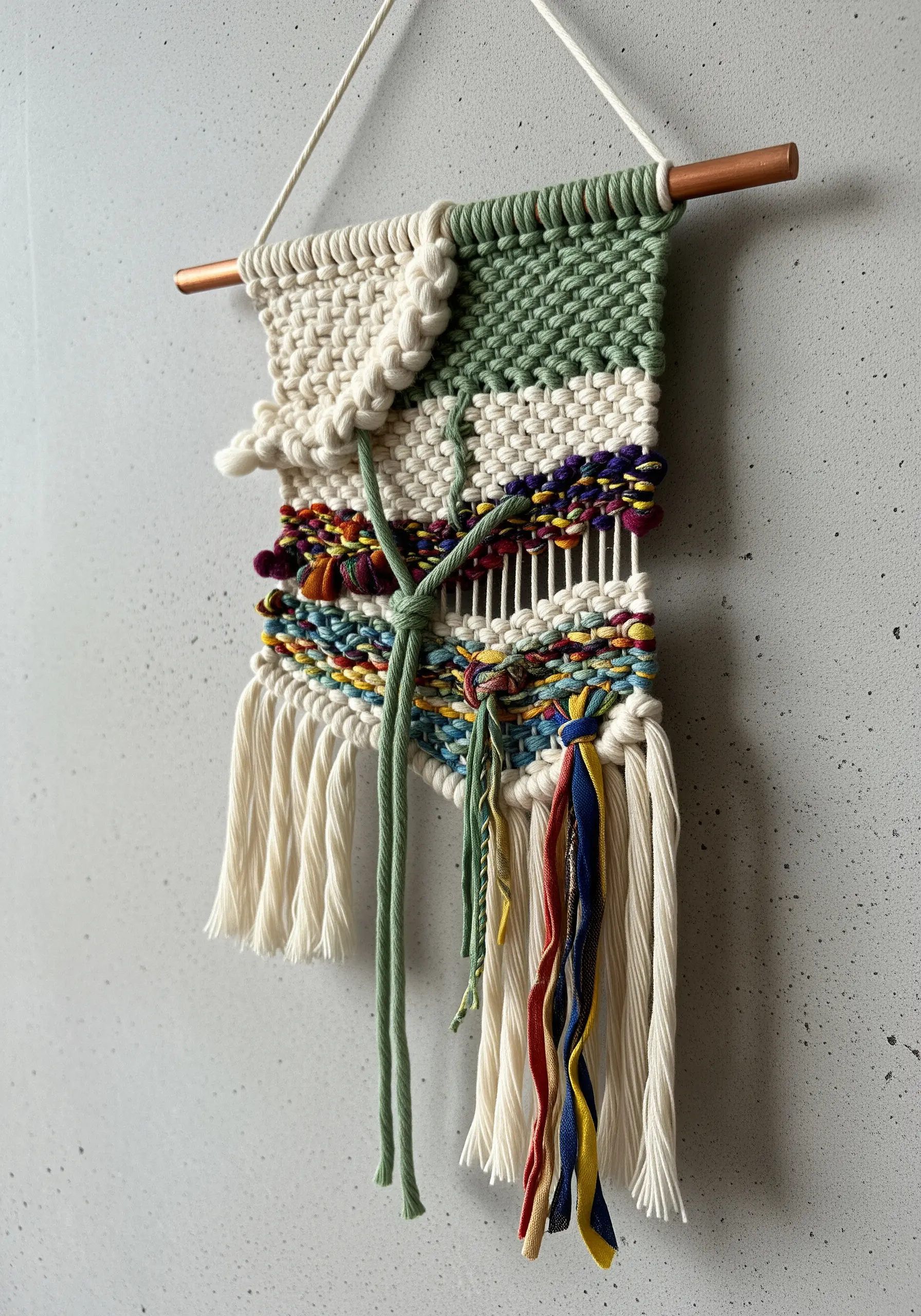 A small, abstract woven wall hanging with mixed fibers, colors, and textures.