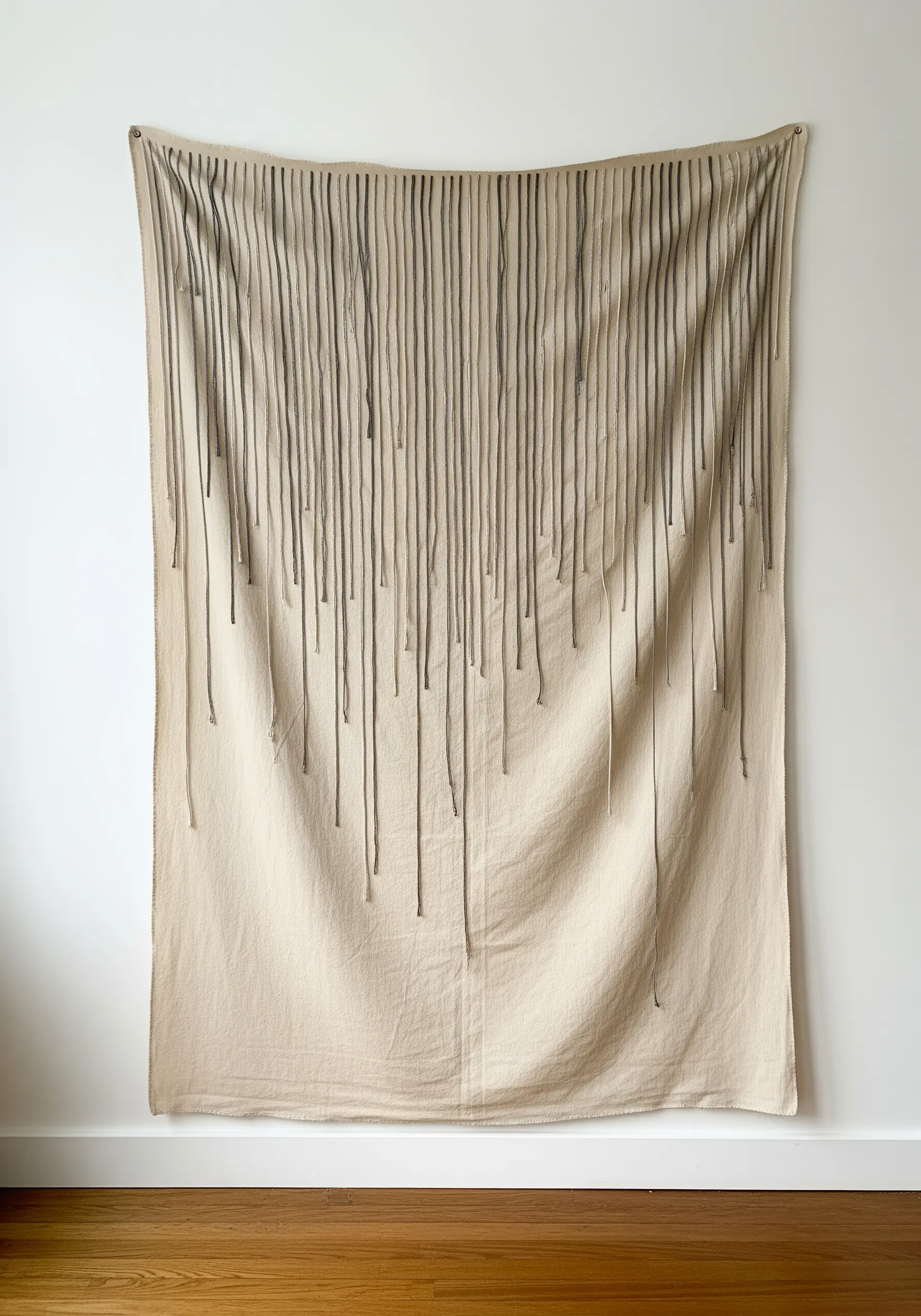 A neutral-colored wall hanging with long threads cascading down from the top.