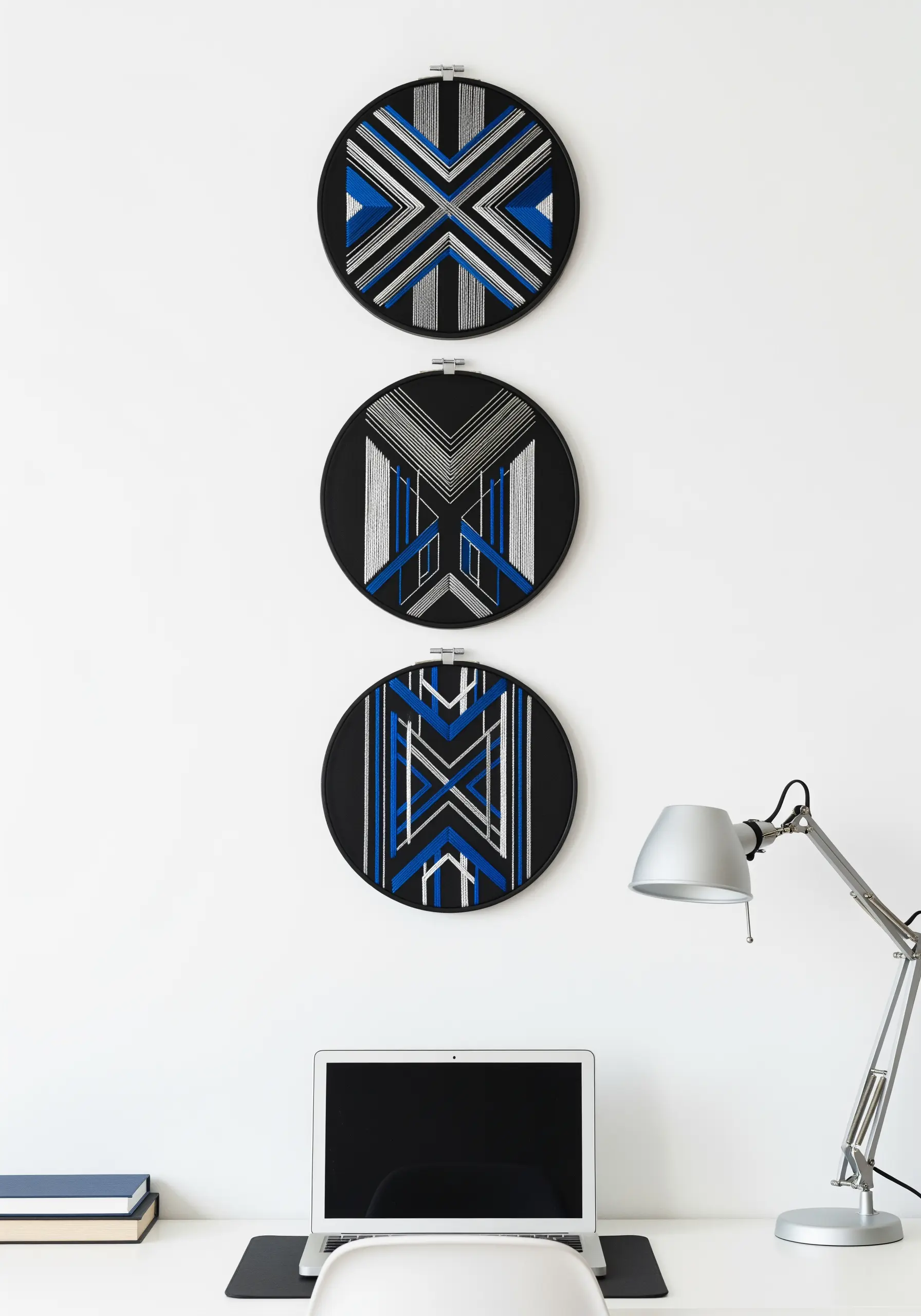Three black embroidery hoops with sharp, symmetrical geometric patterns in blue, silver, and white.