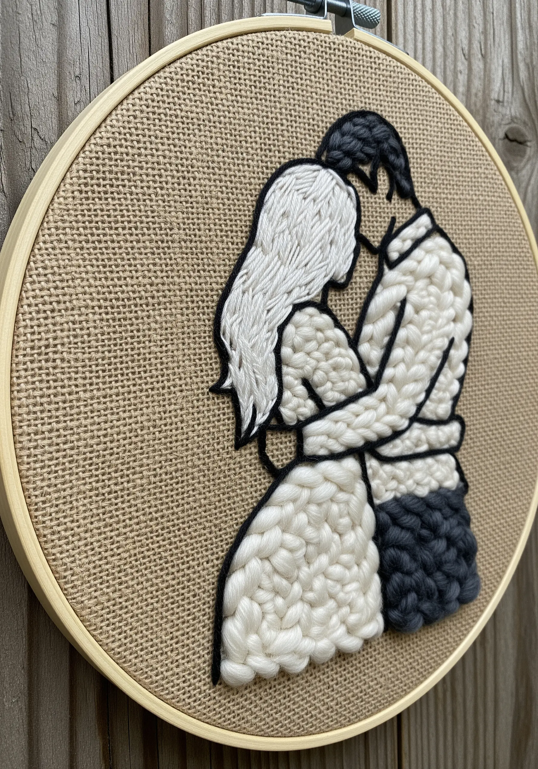A couple's silhouette filled with thick, chunky white and grey yarn on a burlap base.