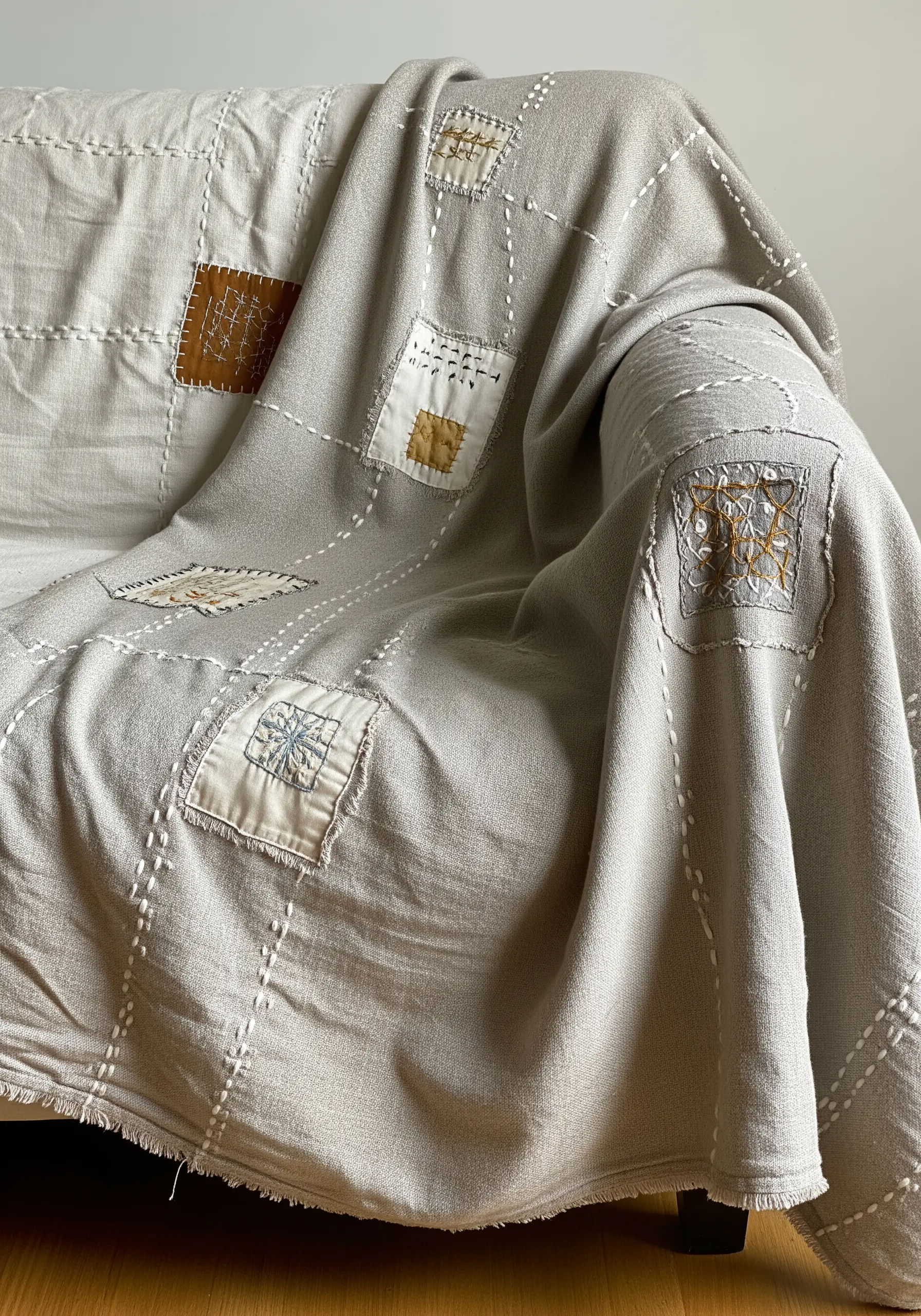 A neutral-toned throw blanket decorated with fabric patches and visible running stitches.