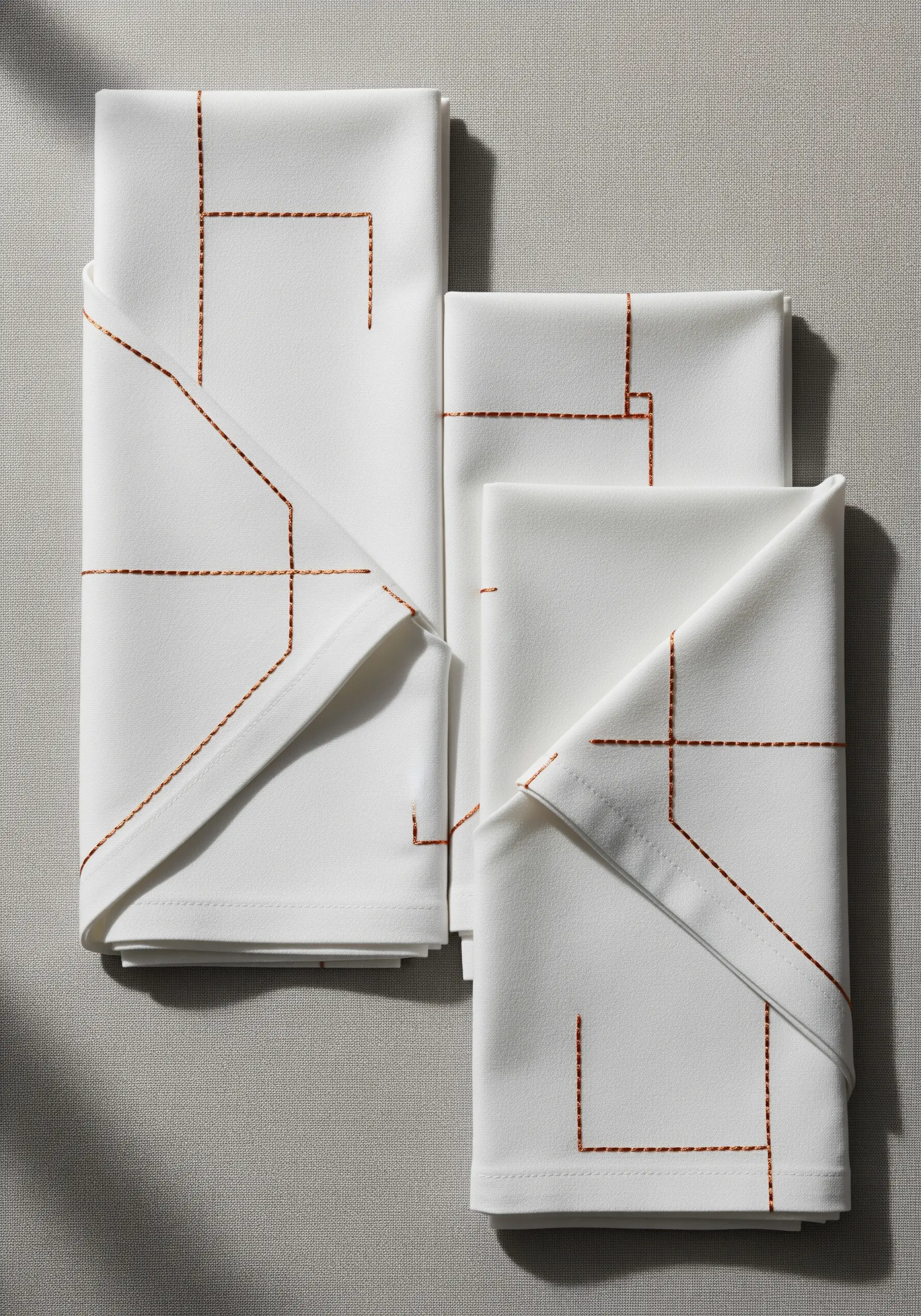 White napkins folded to show minimalist geometric lines embroidered in copper running stitch.