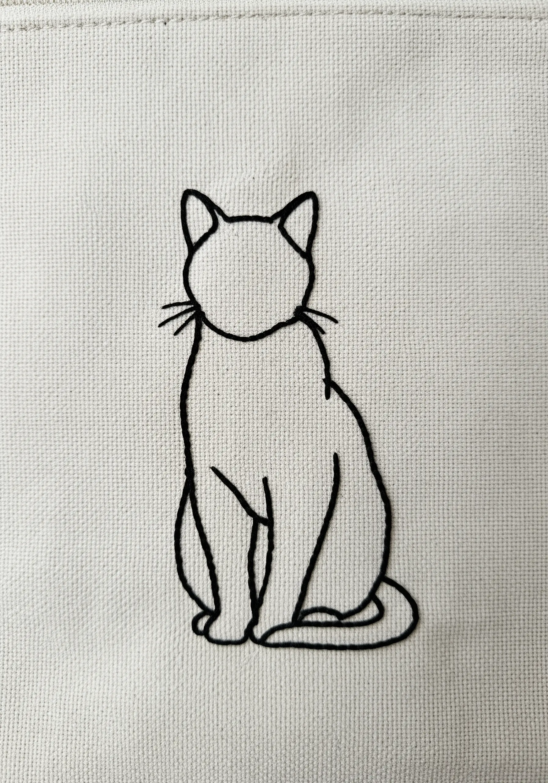 A minimal line art embroidery of a sitting cat, stitched in black thread on a canvas bag.