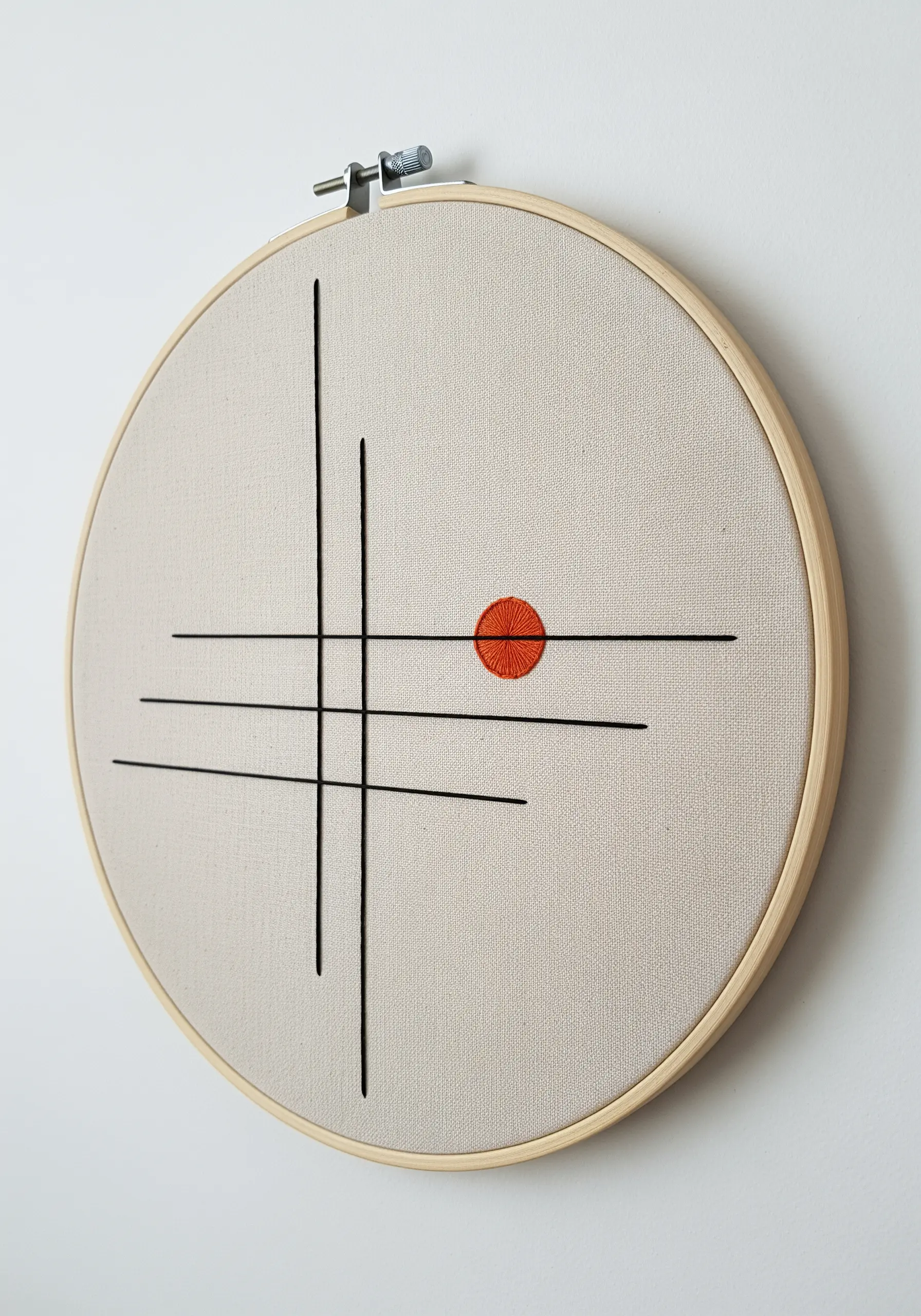 Minimalist black lines intersecting on a neutral background with a single orange satin stitch circle.
