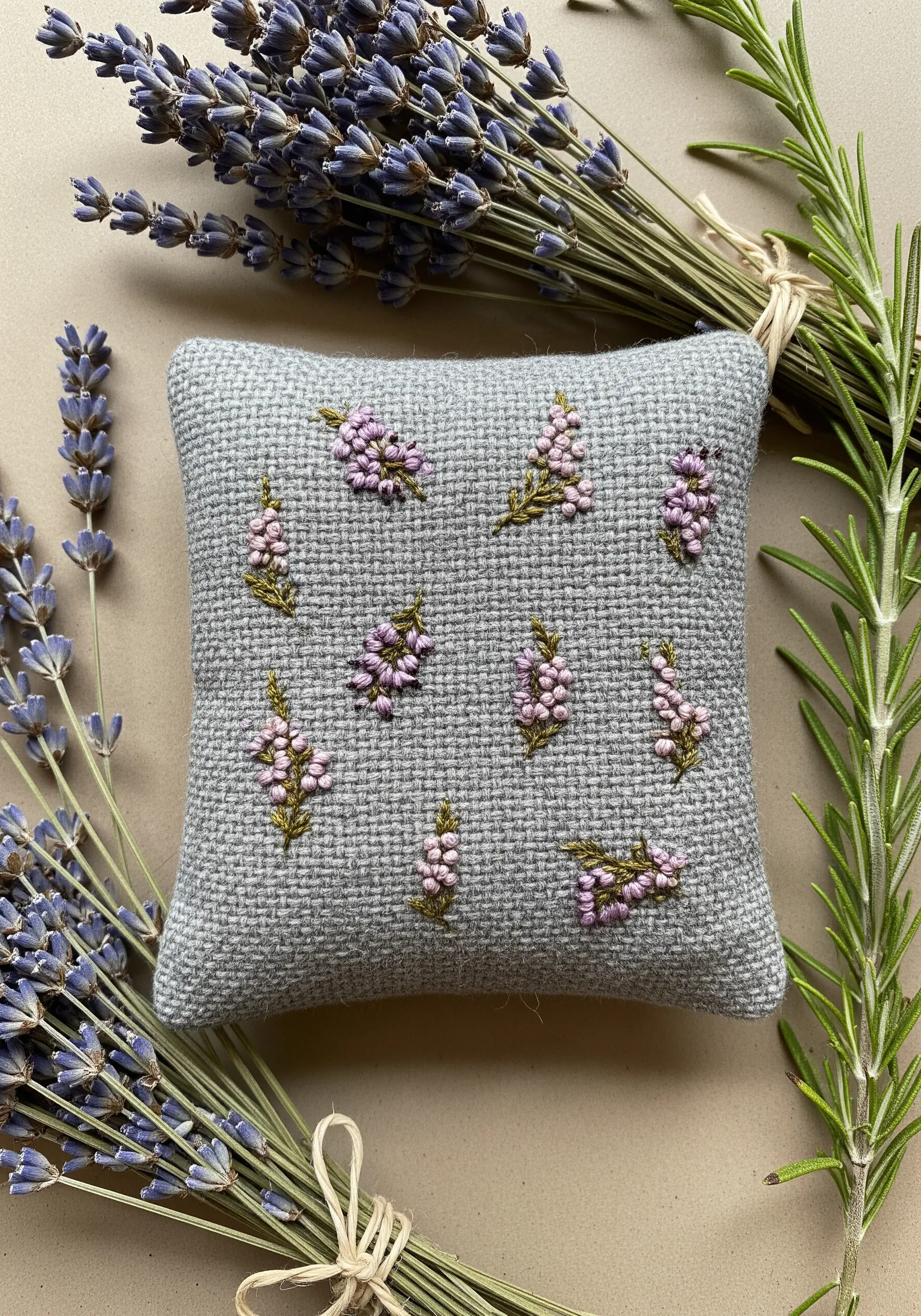 A small gray tweed pillow embroidered with scattered sprigs of pink and purple heather.