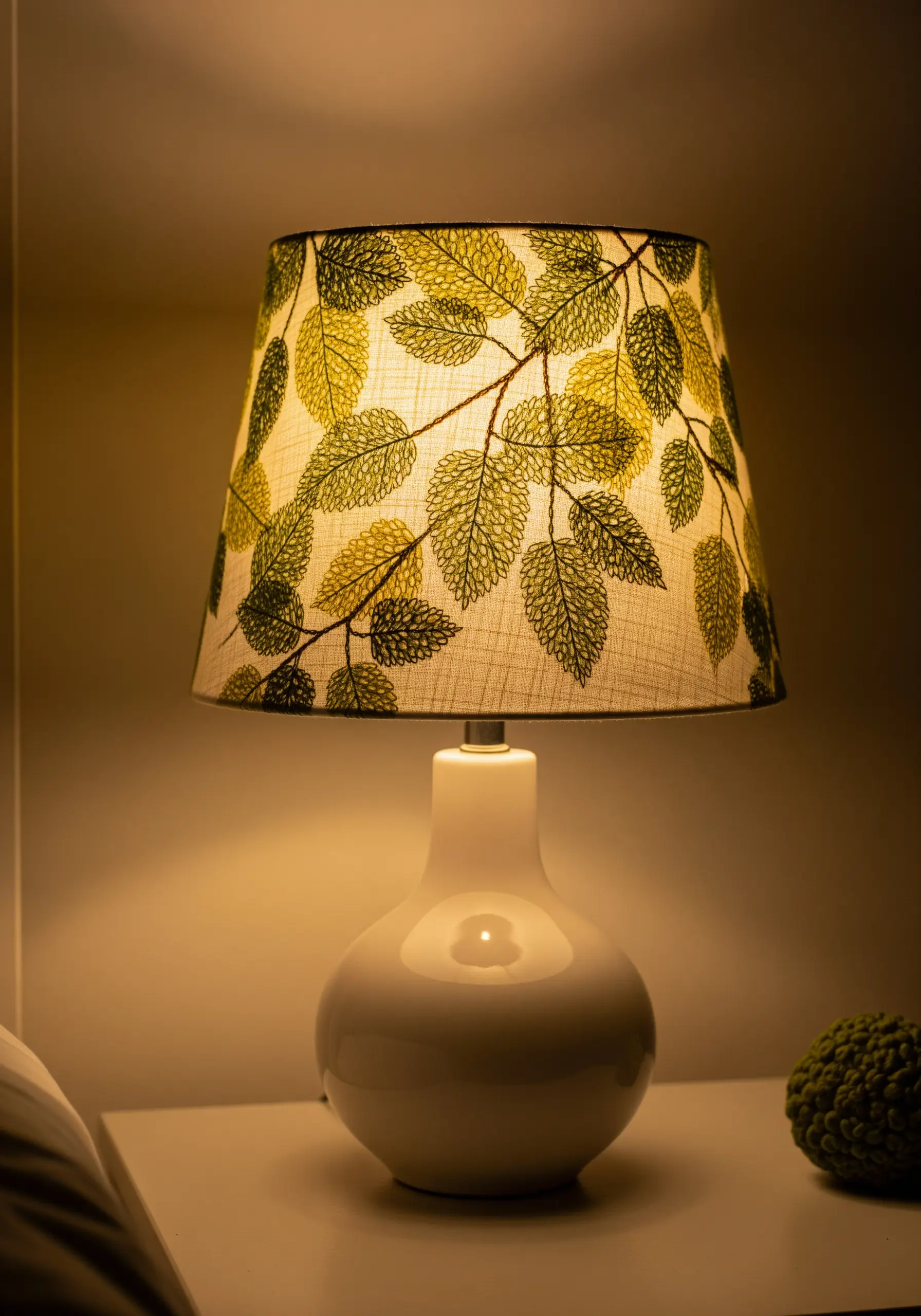 A lampshade embroidered with the delicate vein patterns of leaves, glowing warmly.