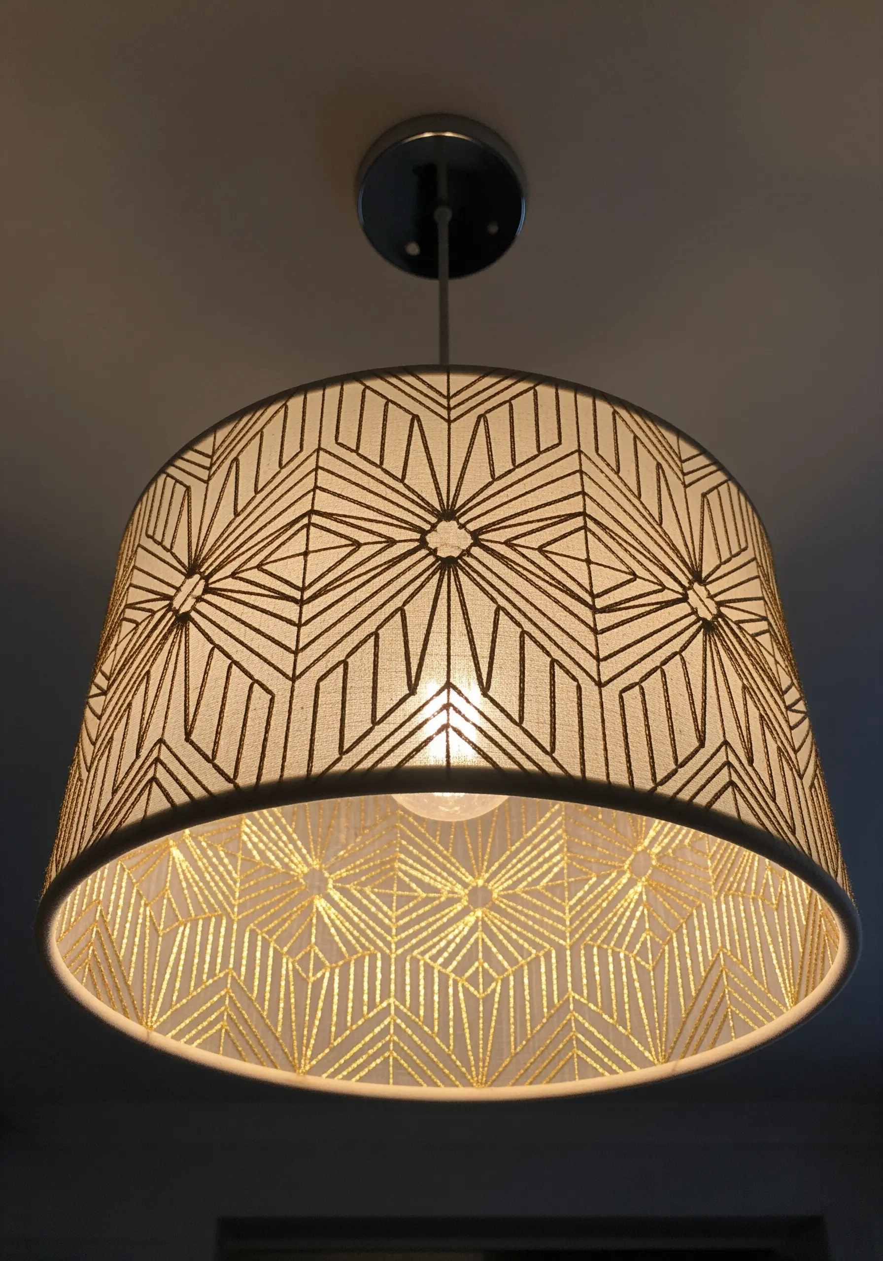 A drum lampshade with a geometric Art Deco pattern embroidered in gold metallic thread.