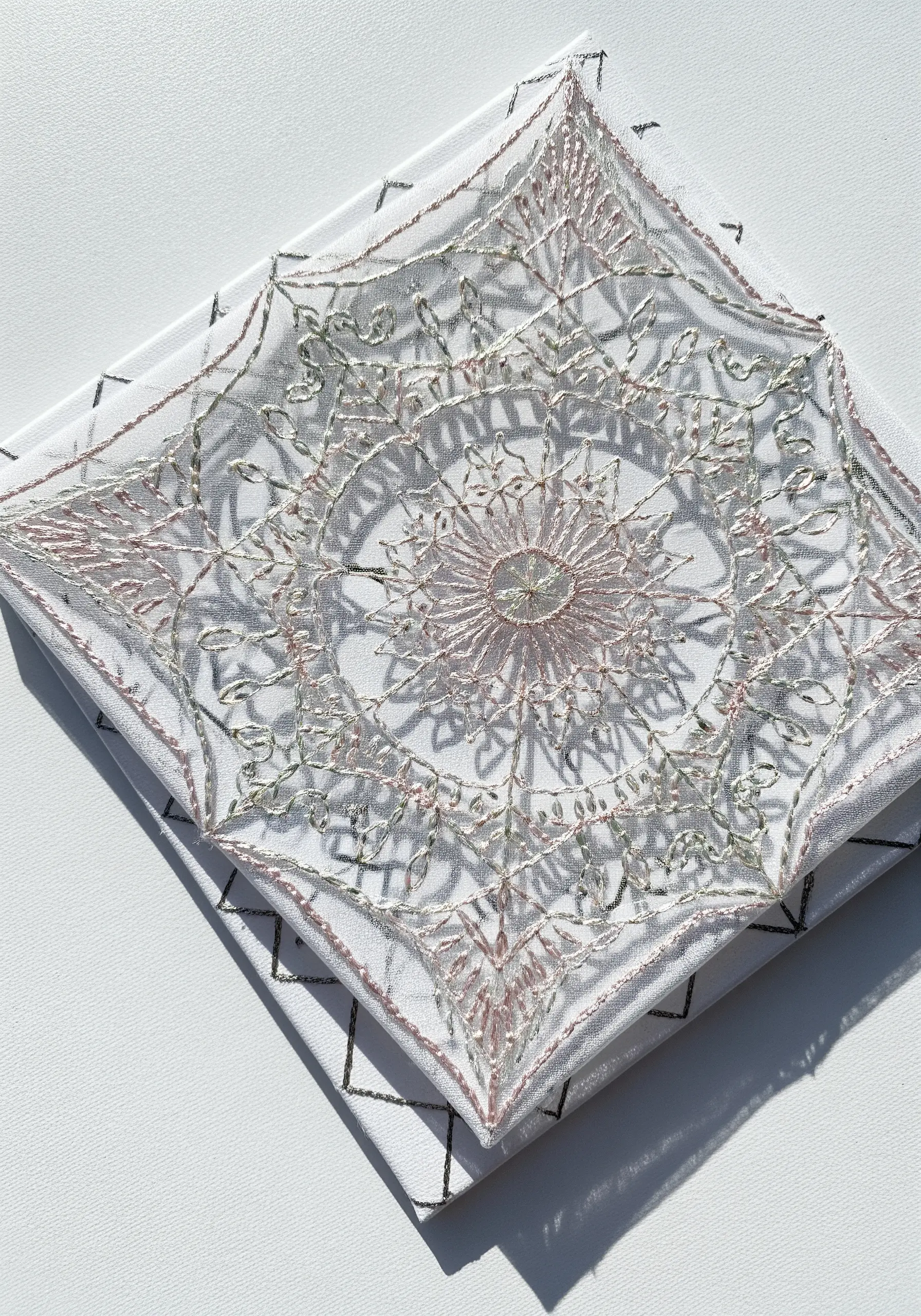 A delicate, intricate mandala stitched with metallic thread on sheer white fabric.