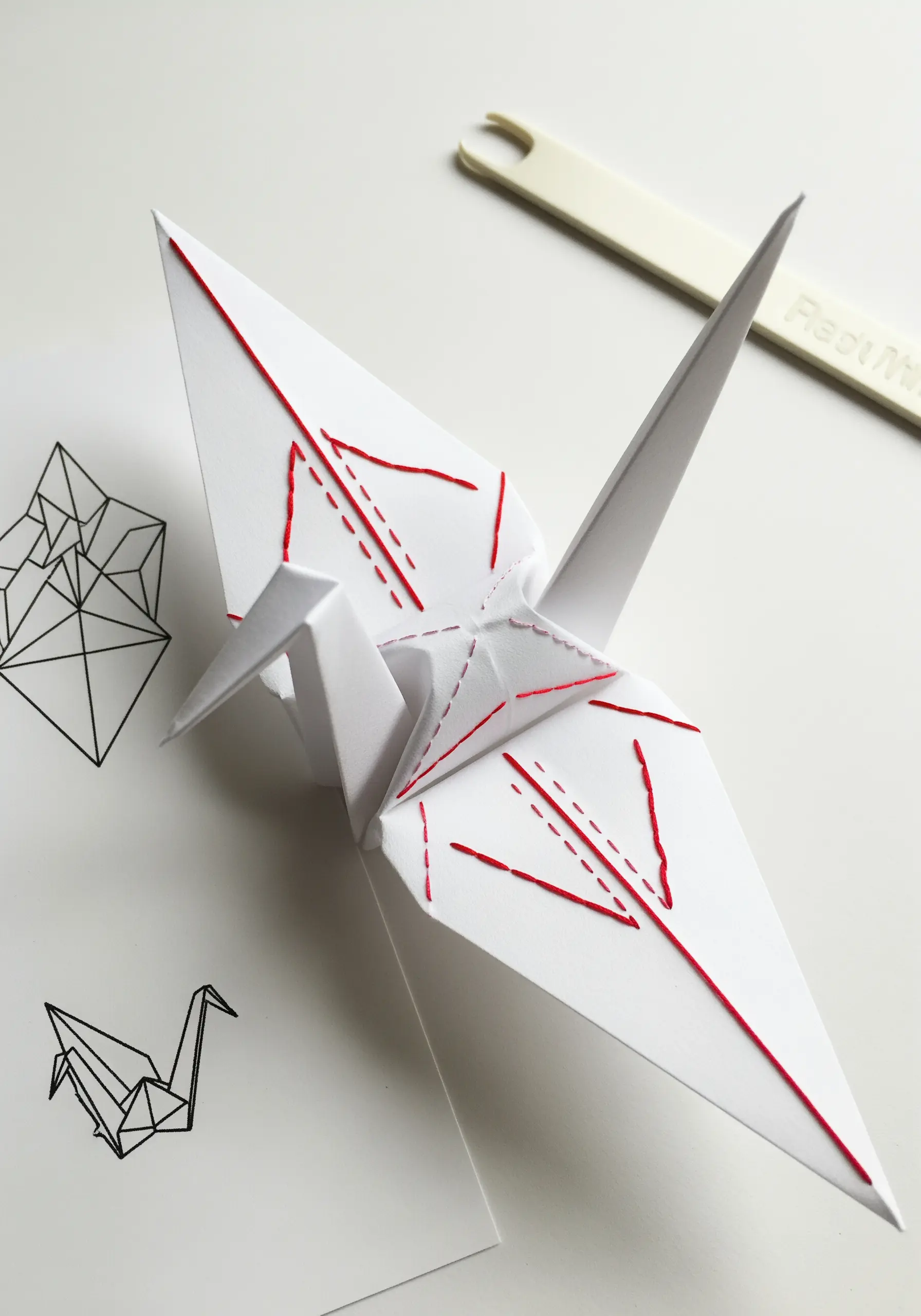 White origami paper crane with red embroidered line details on its wings.