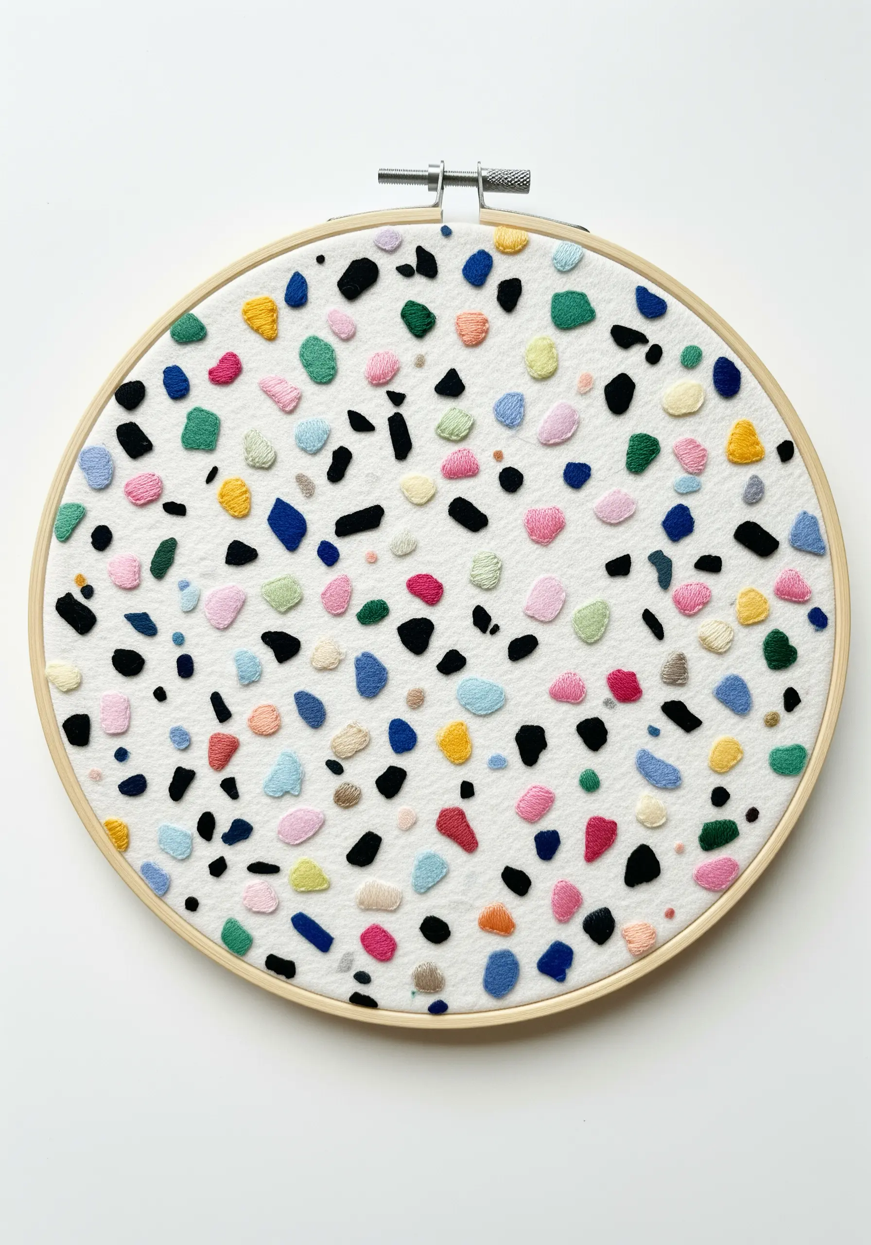 Embroidery that mimics a terrazzo pattern, with small, colorful satin stitch shapes on white fabric.