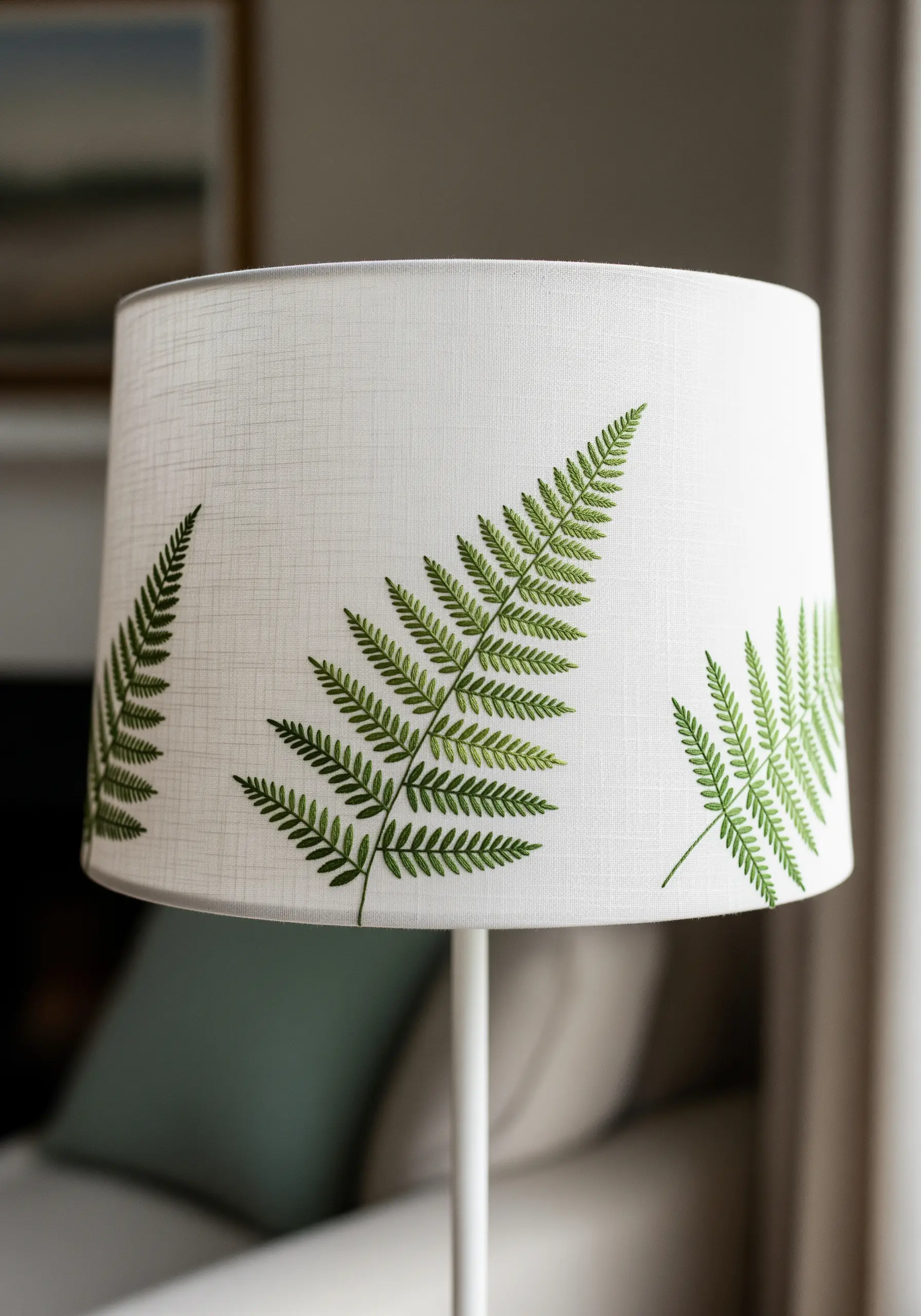 Delicate green fern leaves embroidered around a white fabric lampshade.
