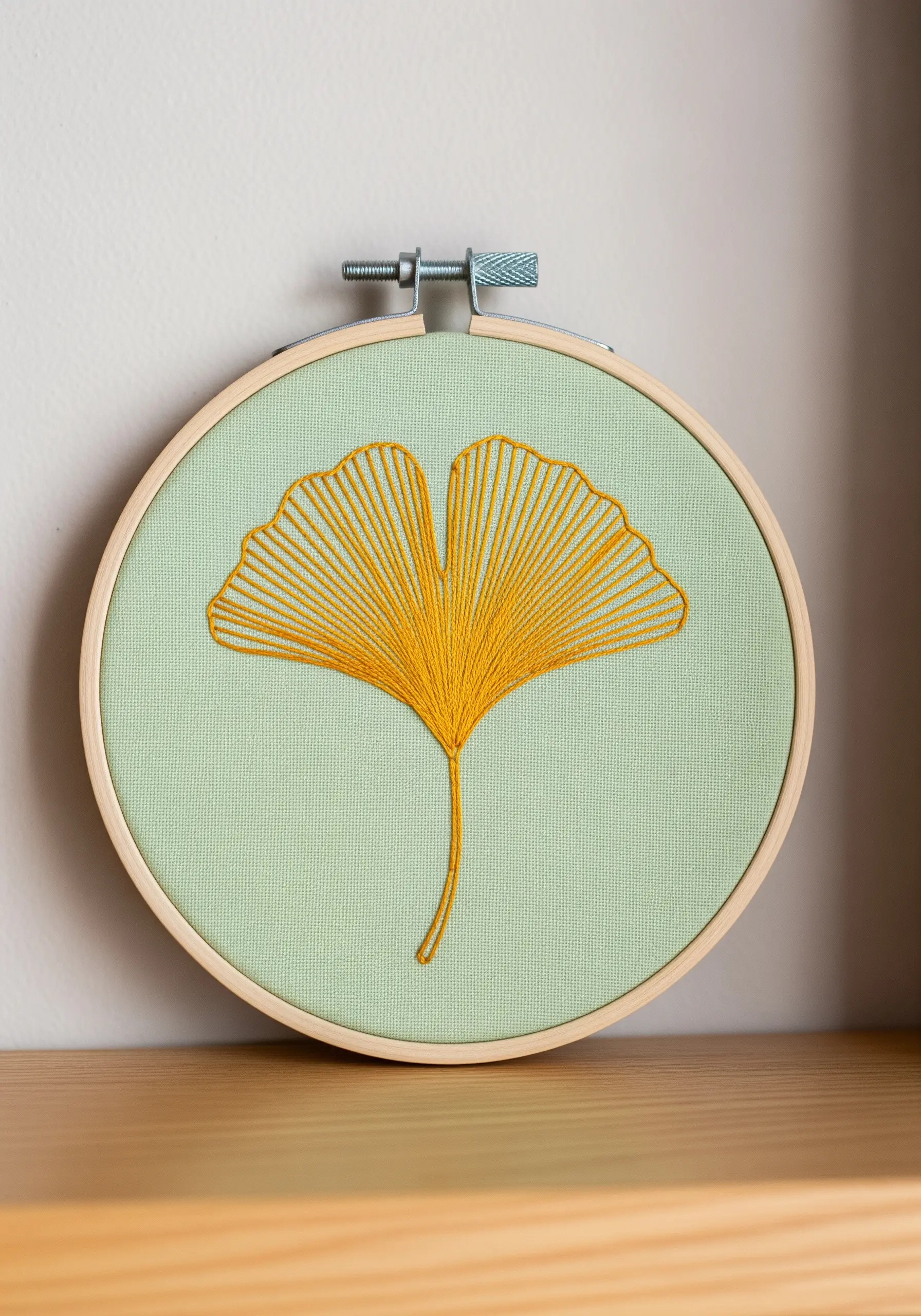 A golden yellow ginkgo leaf embroidered with long, radiating stitches on a mint green background.