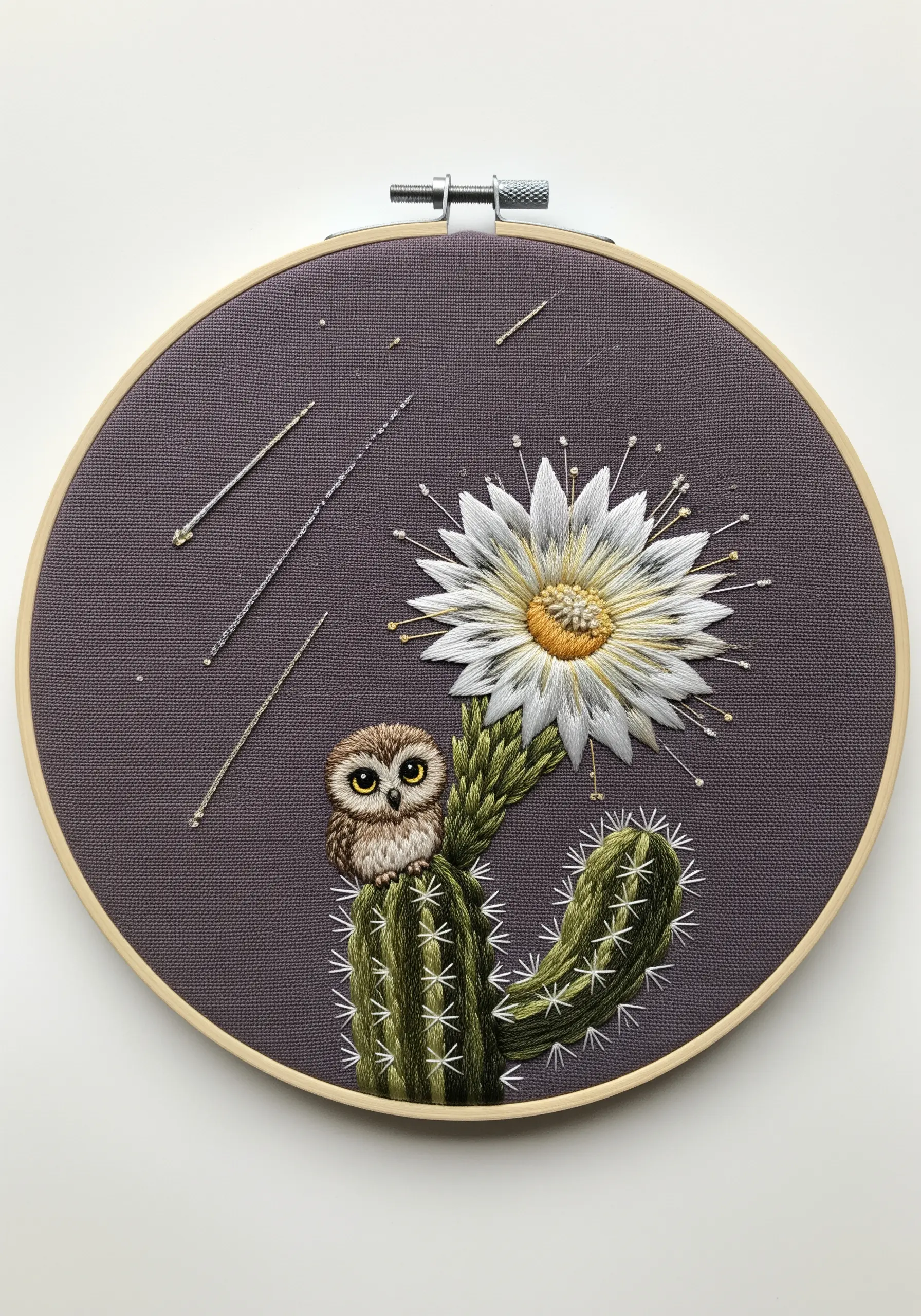 A tiny, detailed owl perched on a large, thread-painted saguaro cactus with a blooming white flower.