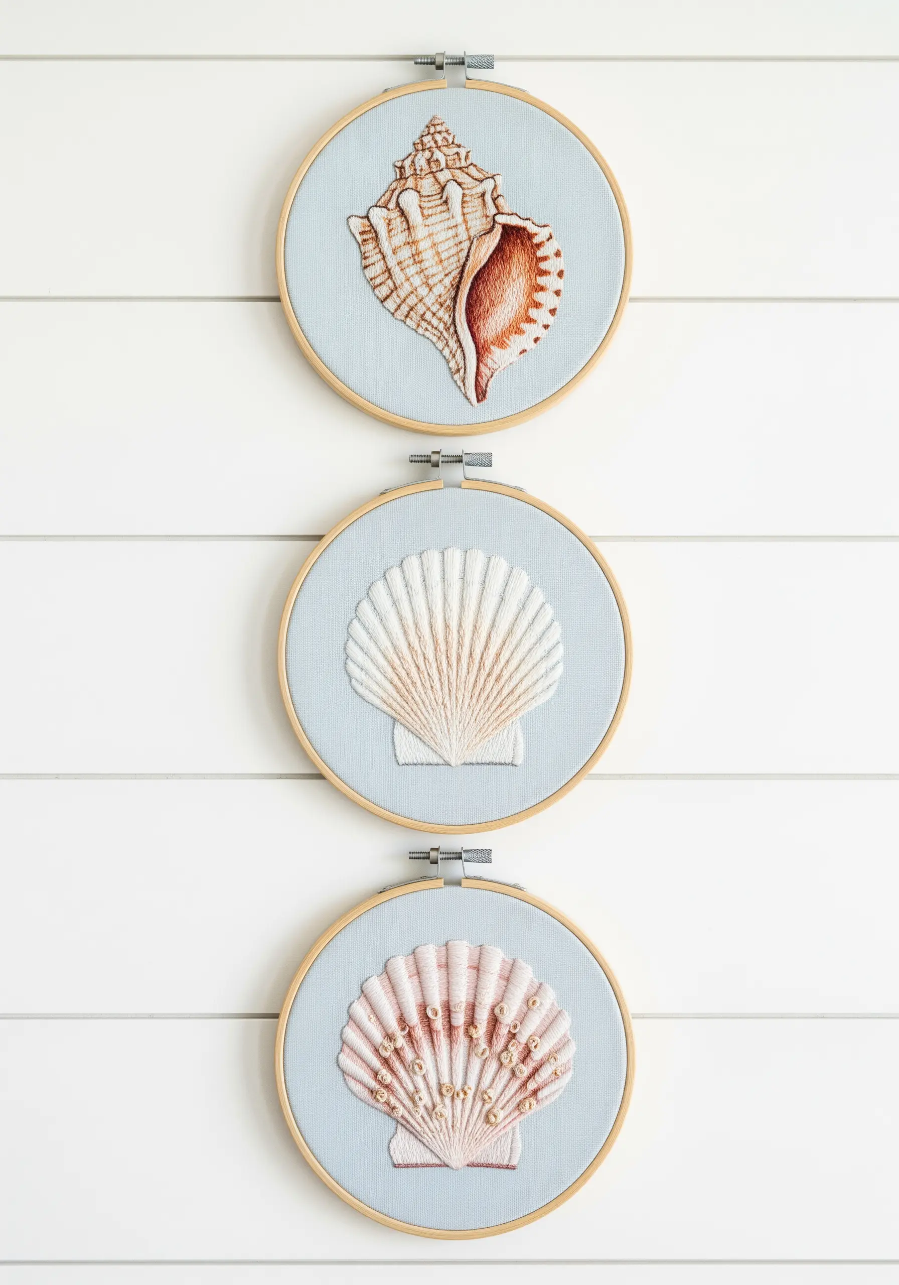 Three embroidery hoops displaying different seashells with realistic shading and texture.