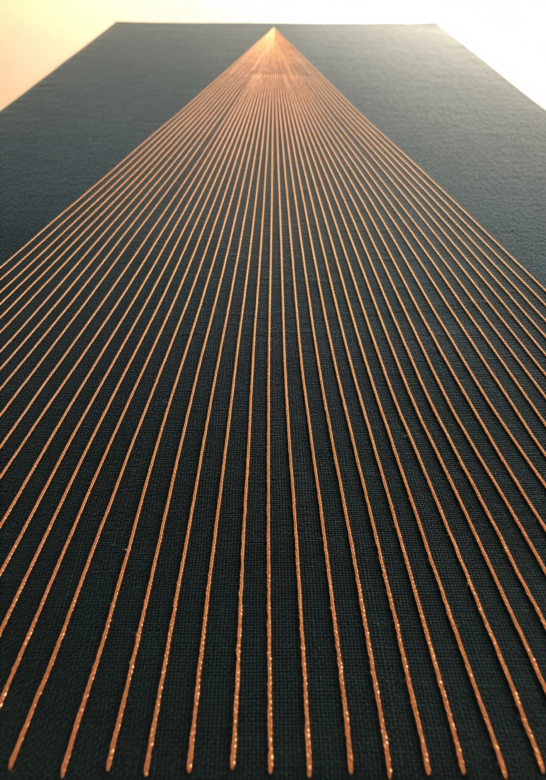 Perspective embroidery with converging golden threads on dark fabric, creating a sense of depth.
