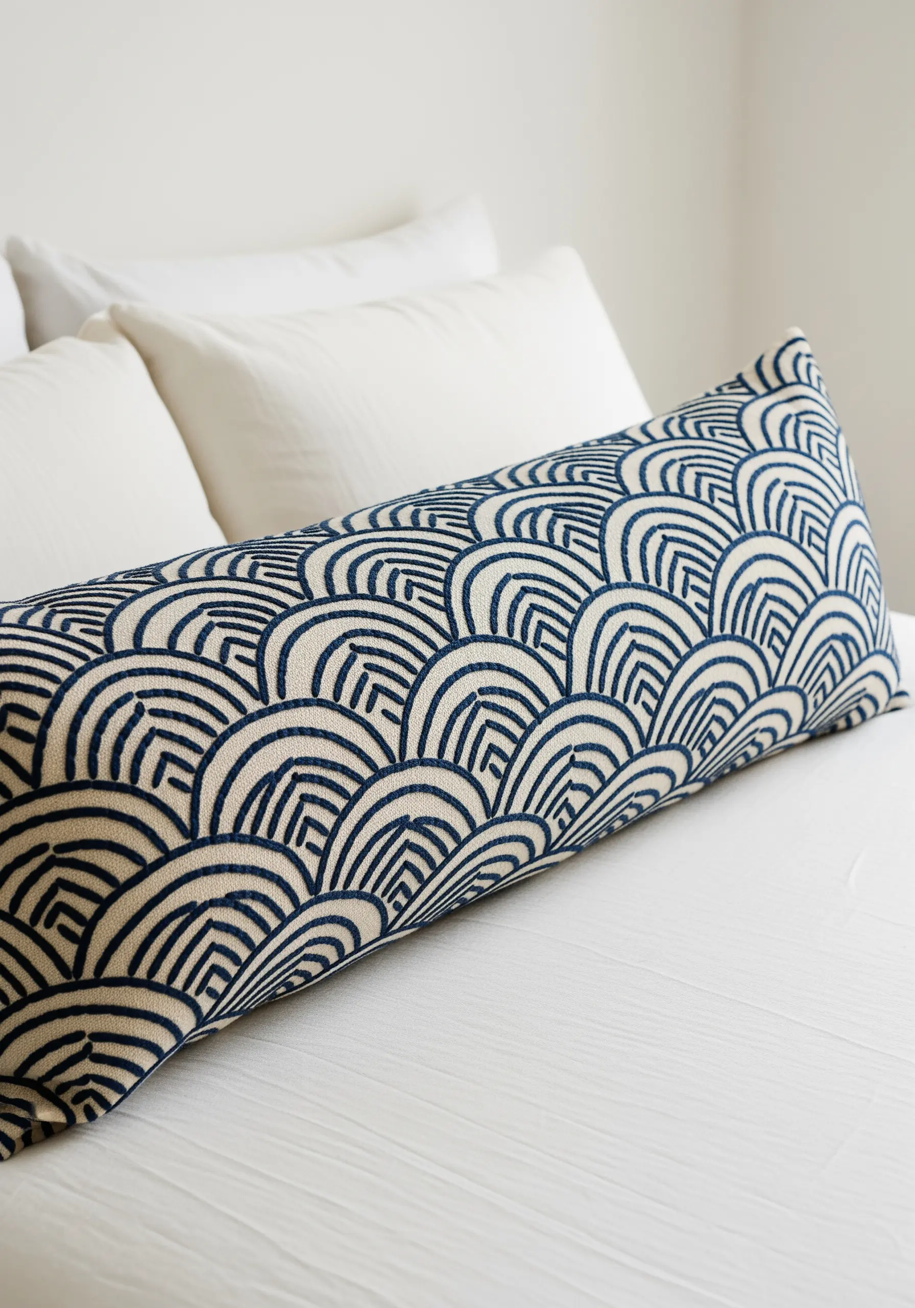 A long pillow embroidered with a repeating geometric Japanese wave pattern in dark blue.