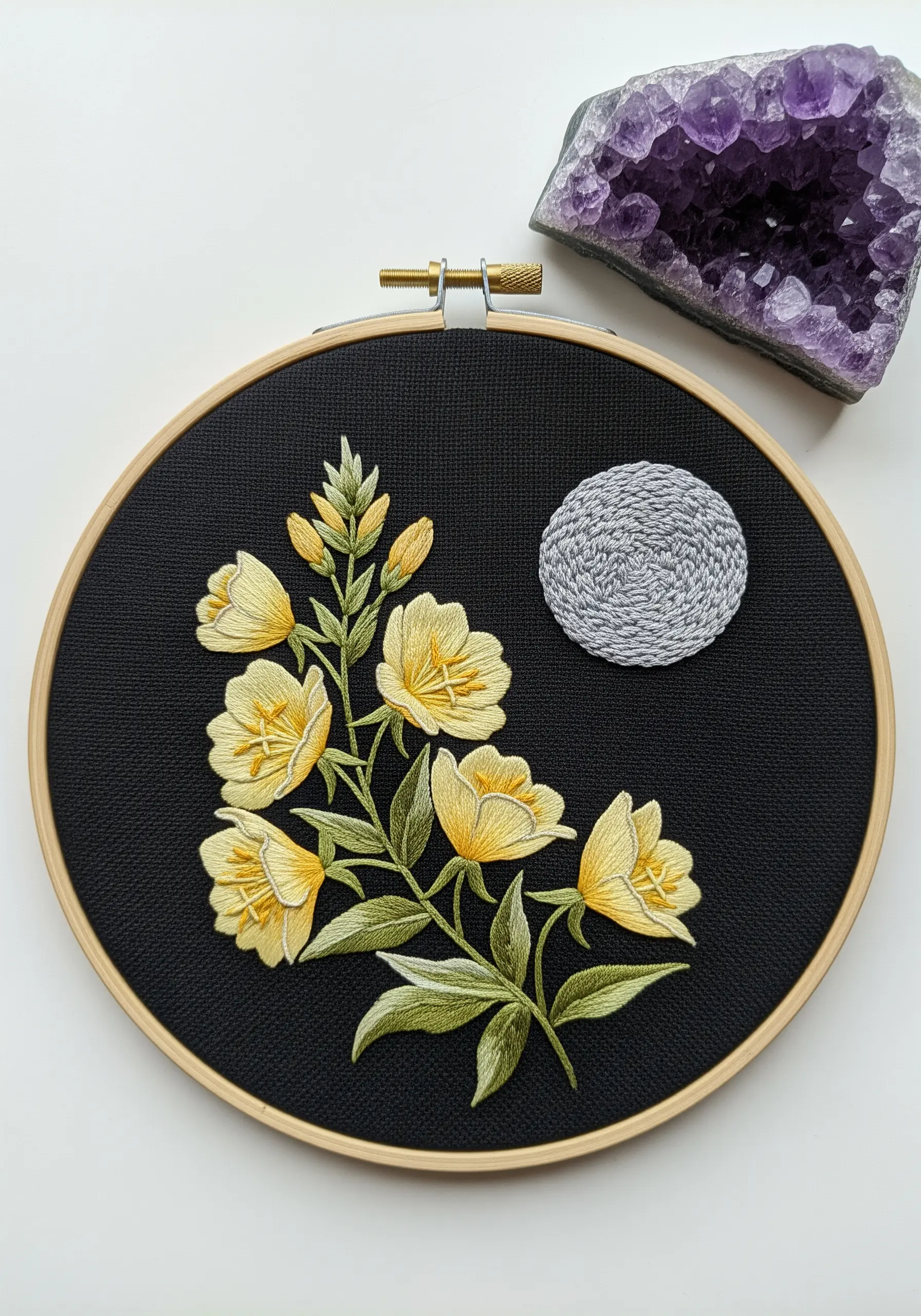 Embroidery of yellow evening primrose flowers next to a textured grey moon on black fabric.