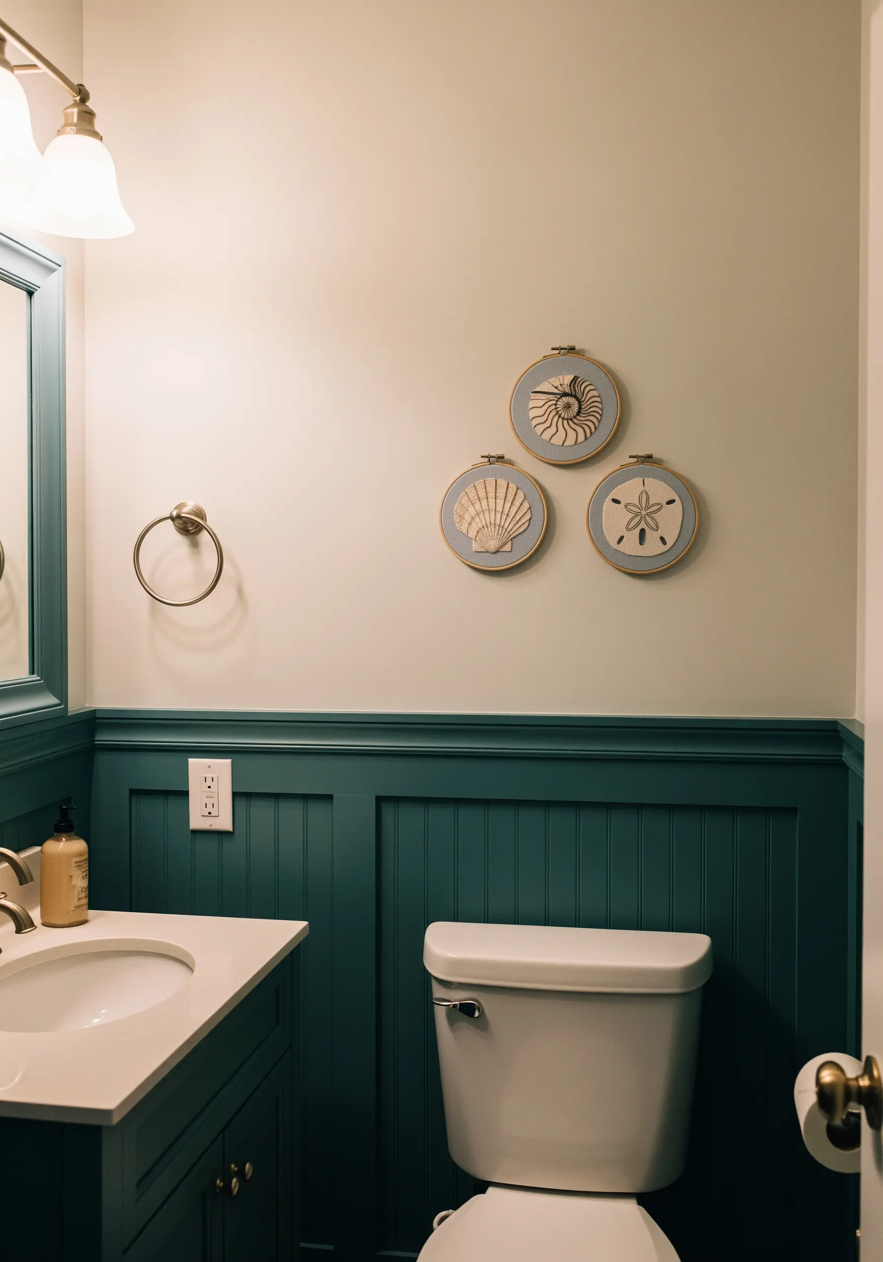 Three embroidery hoops with detailed seashell motifs hanging in a teal and white bathroom.
