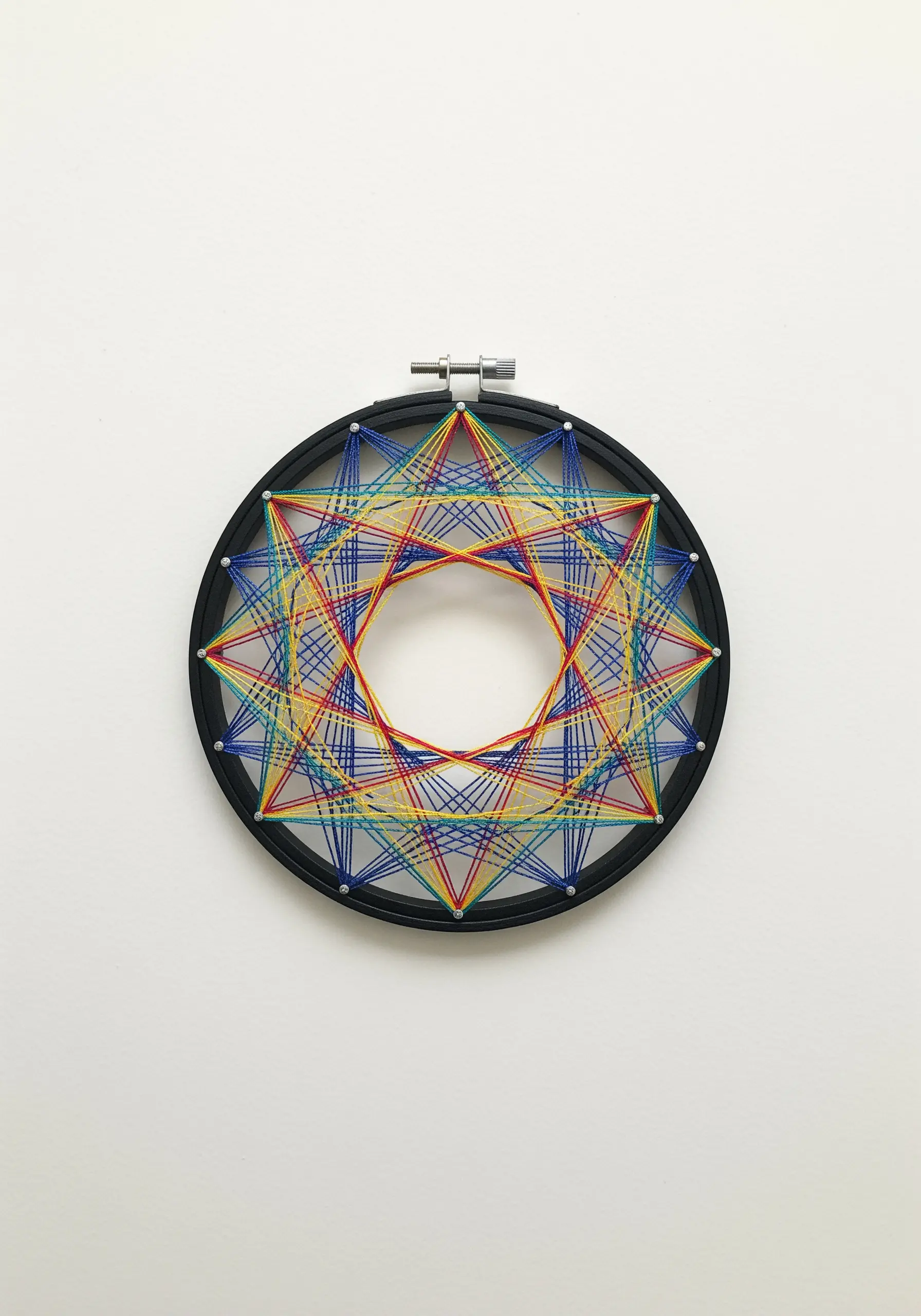 Geometric string art made with colorful threads stretched across a black hoop.