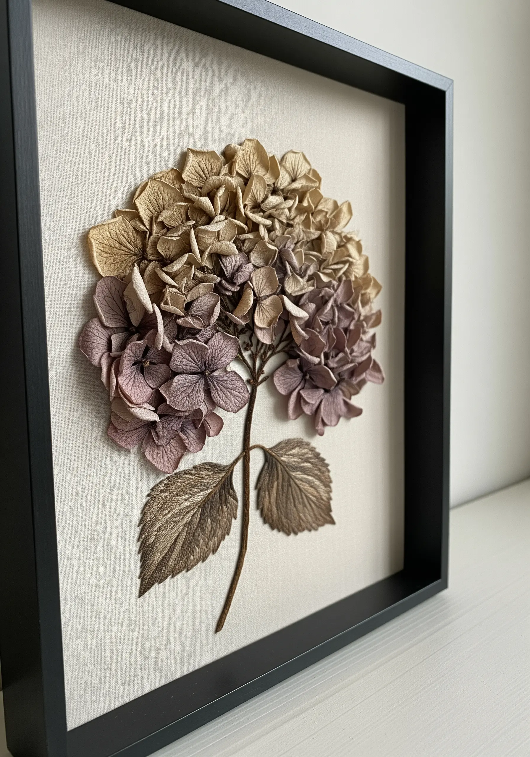 A framed, sculptural hydrangea made from layered, cut paper or fabric in muted brown and mauve tones.