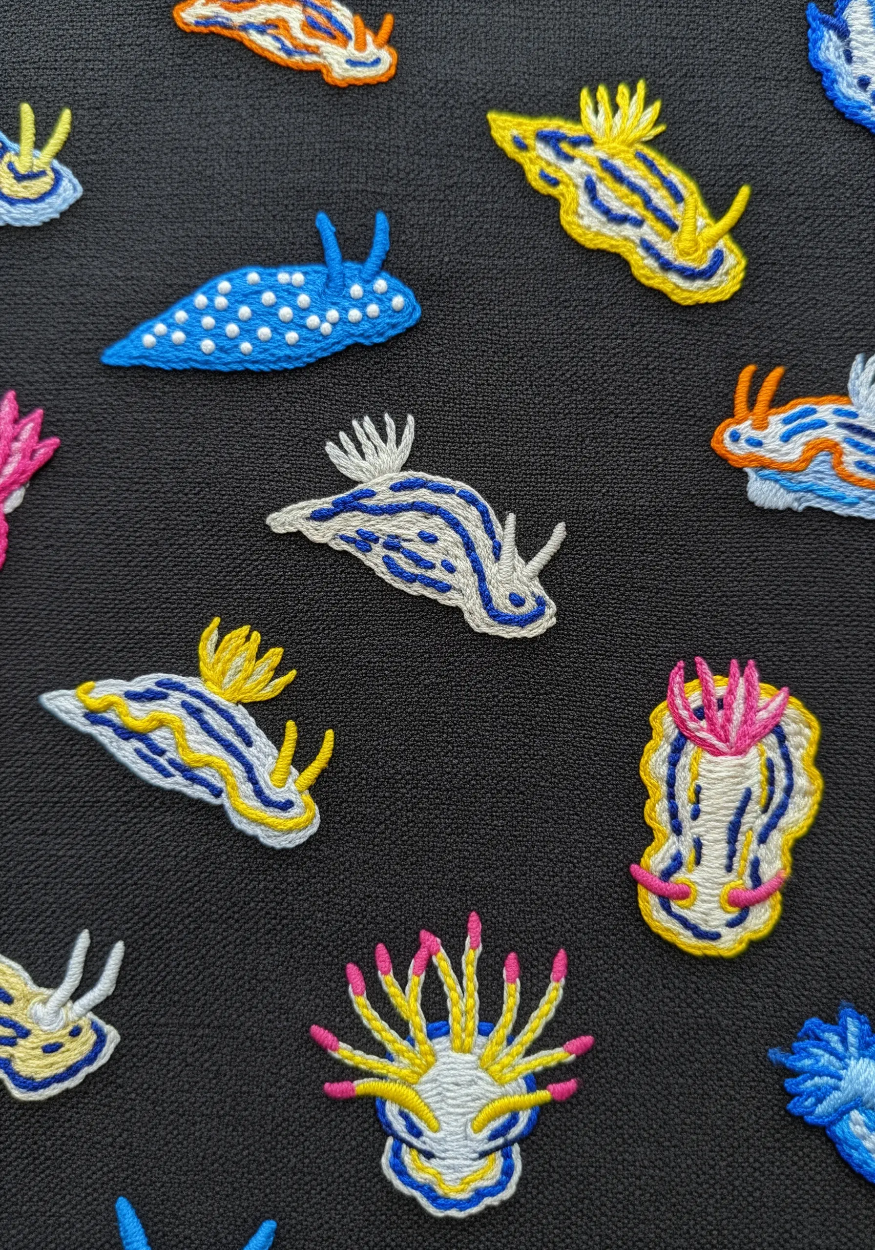 A collection of brightly colored nudibranch sea slugs embroidered on black fabric.