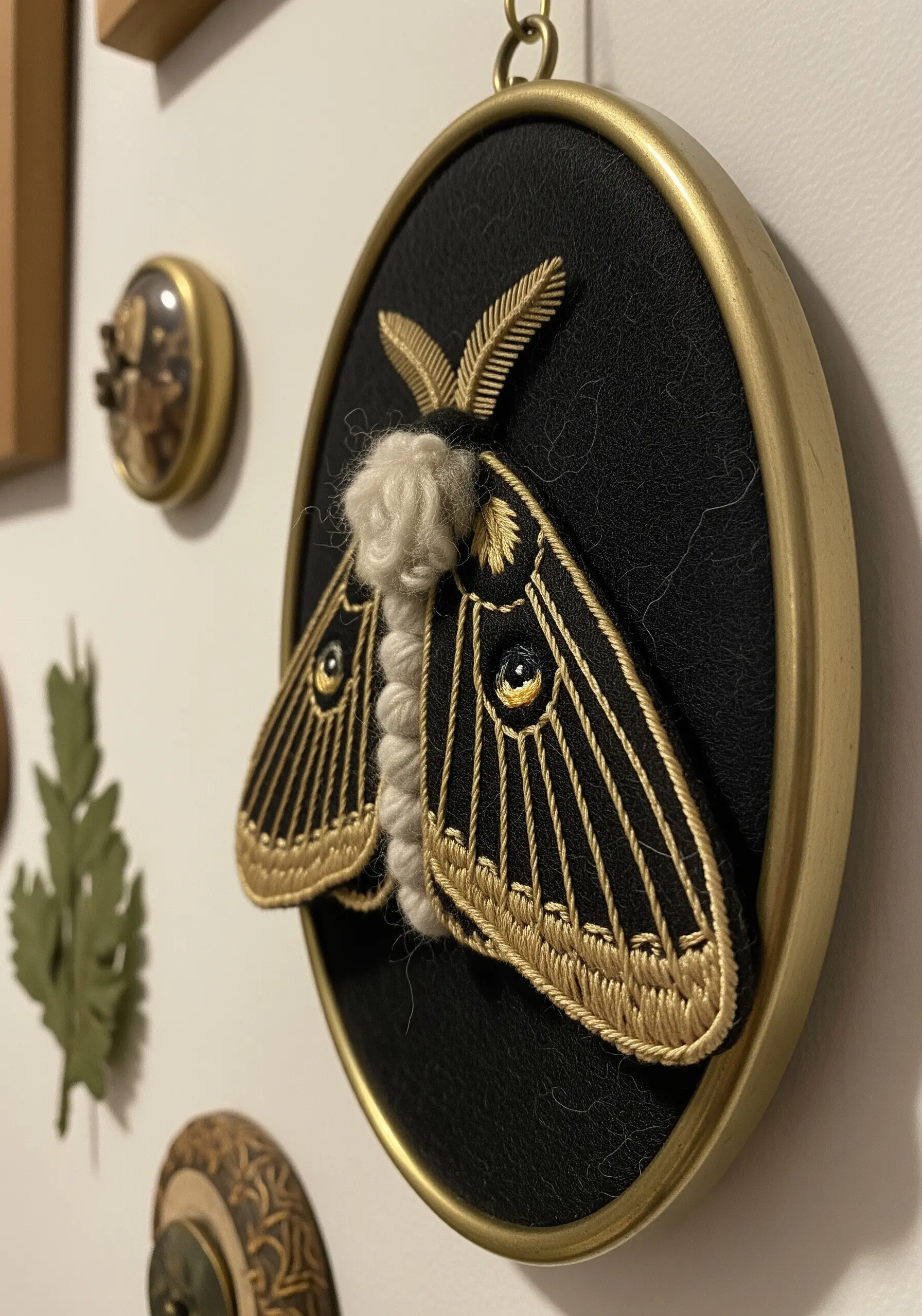A 3D stumpwork embroidery of a moth with raised wings and a fuzzy body, on black fabric.