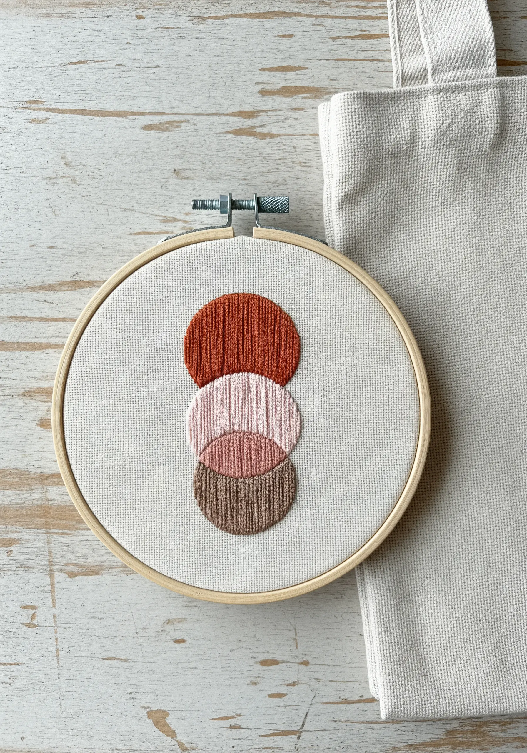 An abstract design of three stacked, overlapping circles in earthy tones in an embroidery hoop.