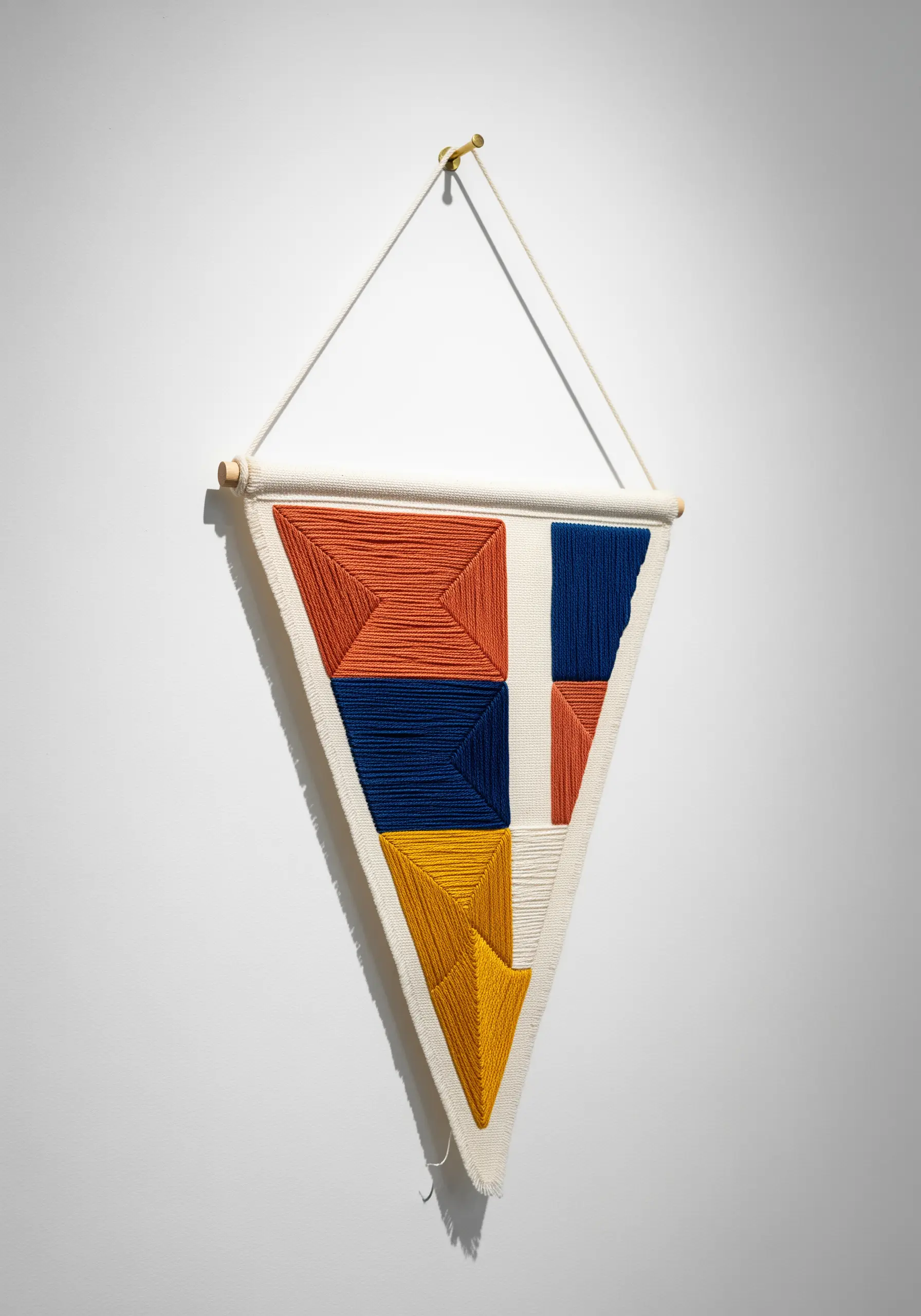 Geometric color-block wall hanging made with couched yarn in a triangle shape.