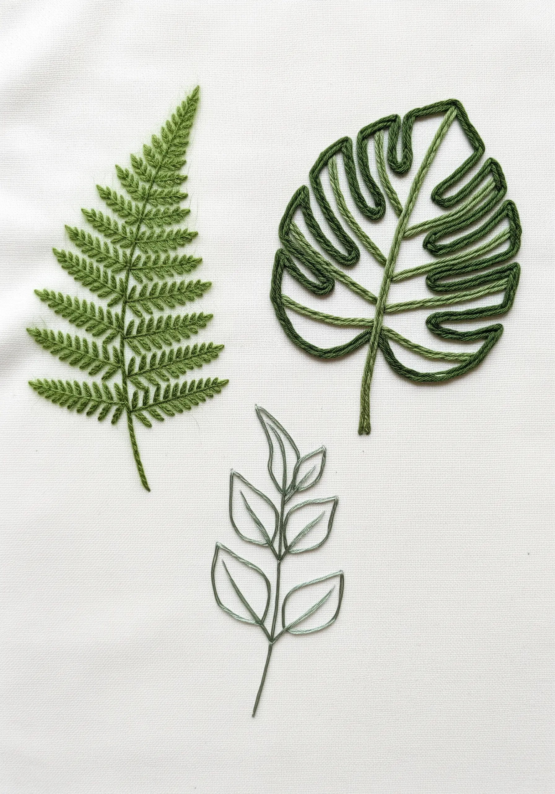 Three different embroidered leaf styles: a filled fern, a yarn outline monstera, and a wire leaf.