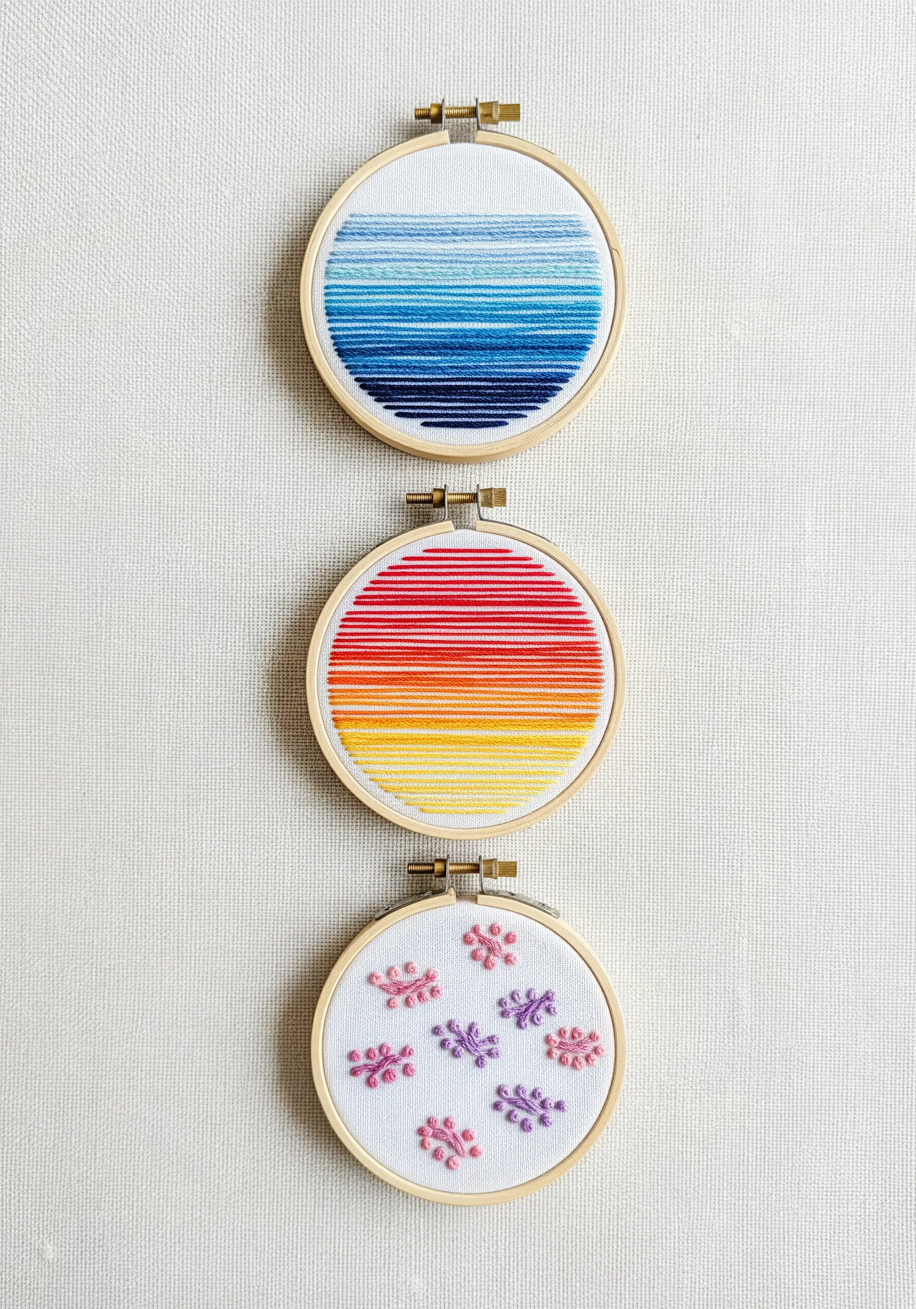 Three small embroidery hoops displaying different abstract color gradient patterns.