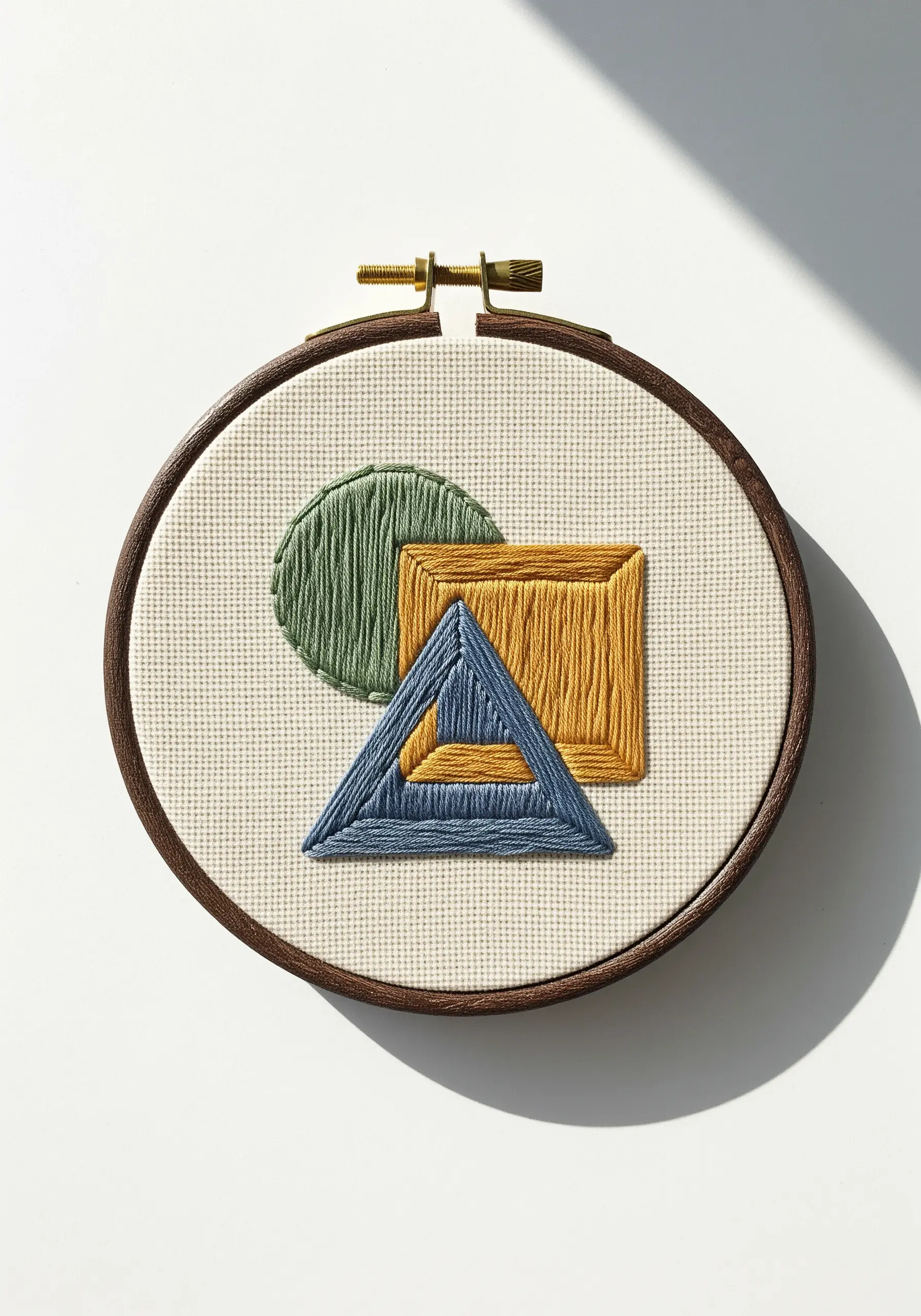 Overlapping geometric shapes filled with satin stitches in green, yellow, and blue.