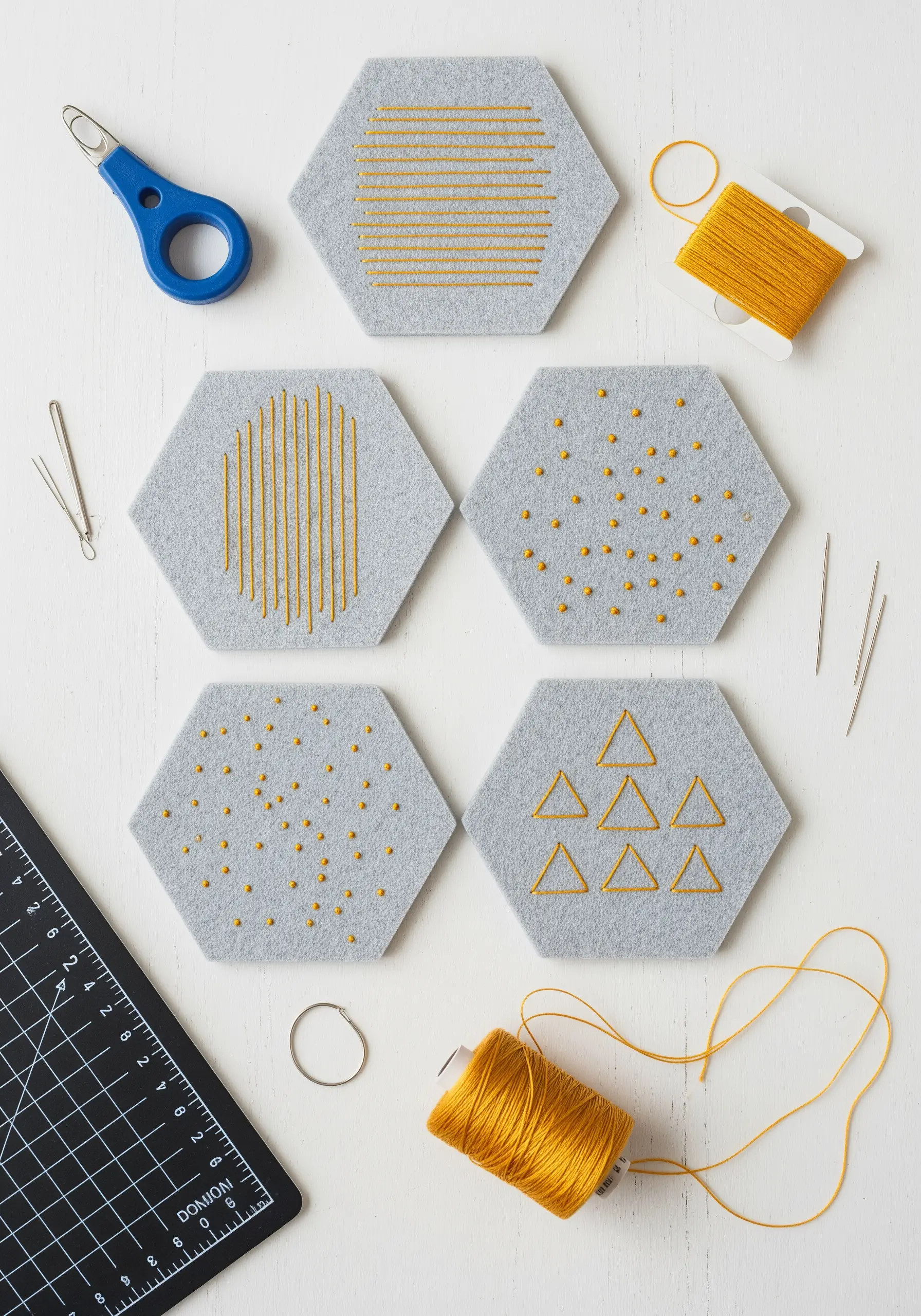 Hexagonal felt coasters with geometric patterns in yellow thread.