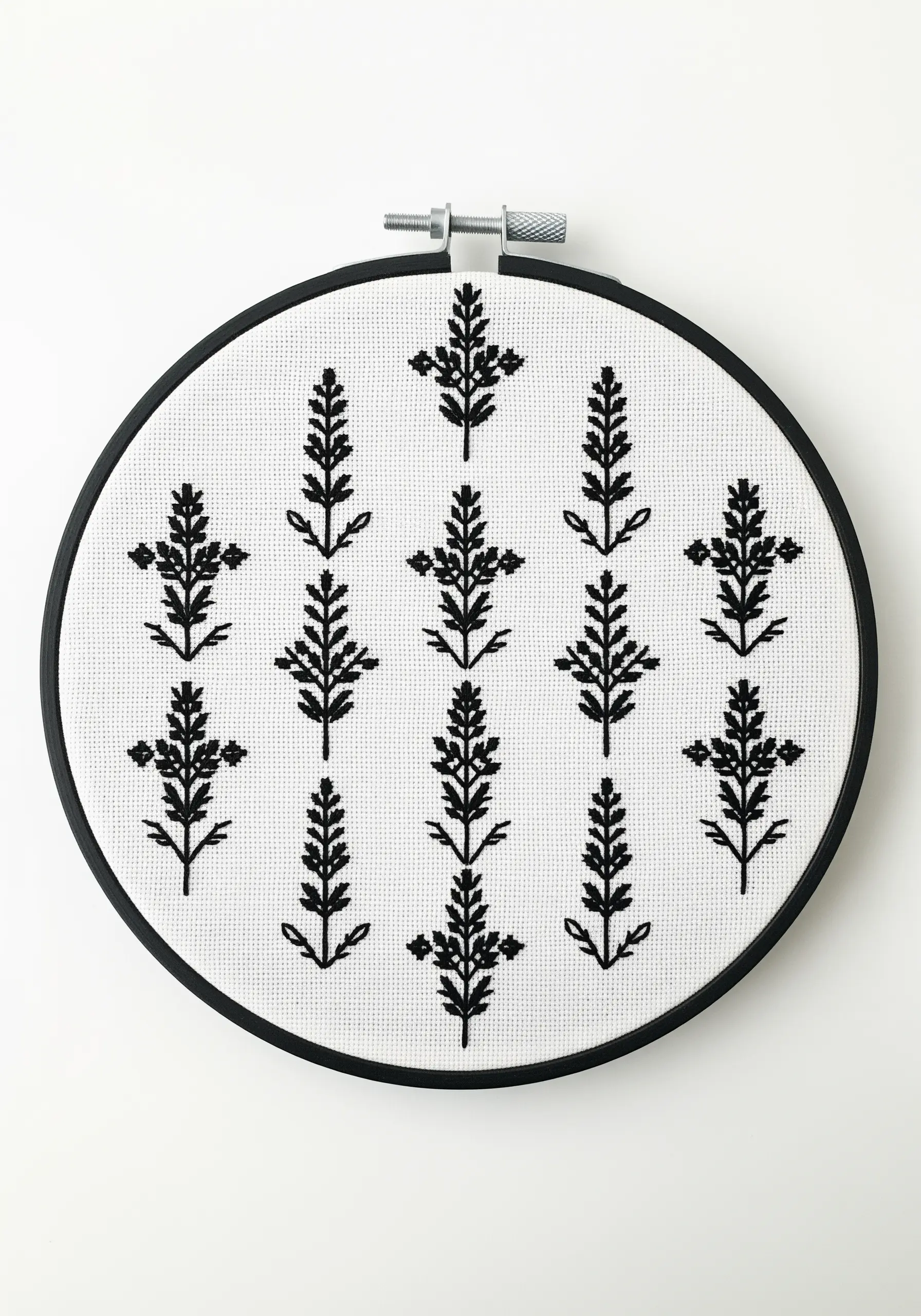 A blackwork embroidery pattern of repeating lavender sprigs in a black hoop.