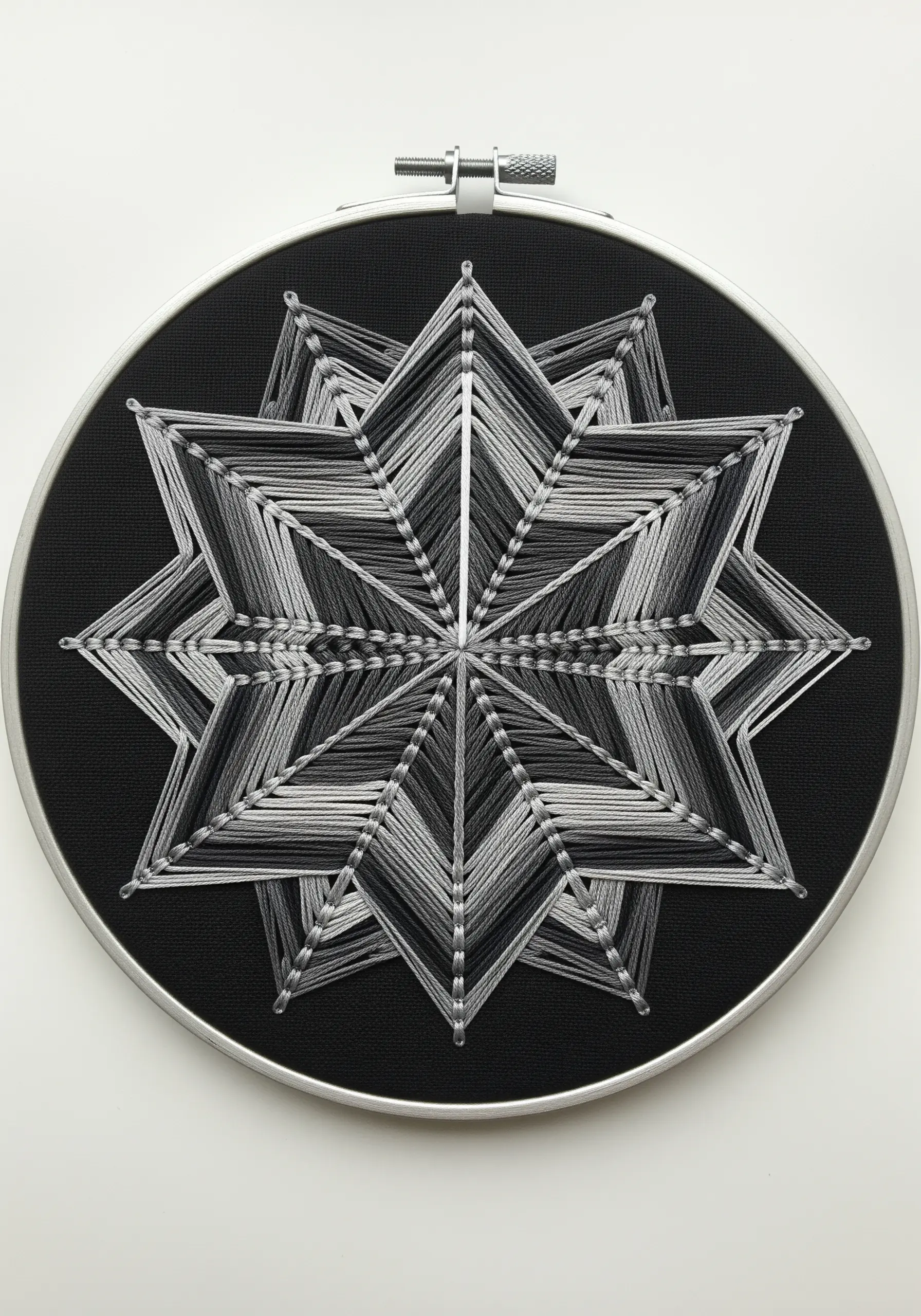 Monochromatic string art star mandala in grayscale on black fabric.