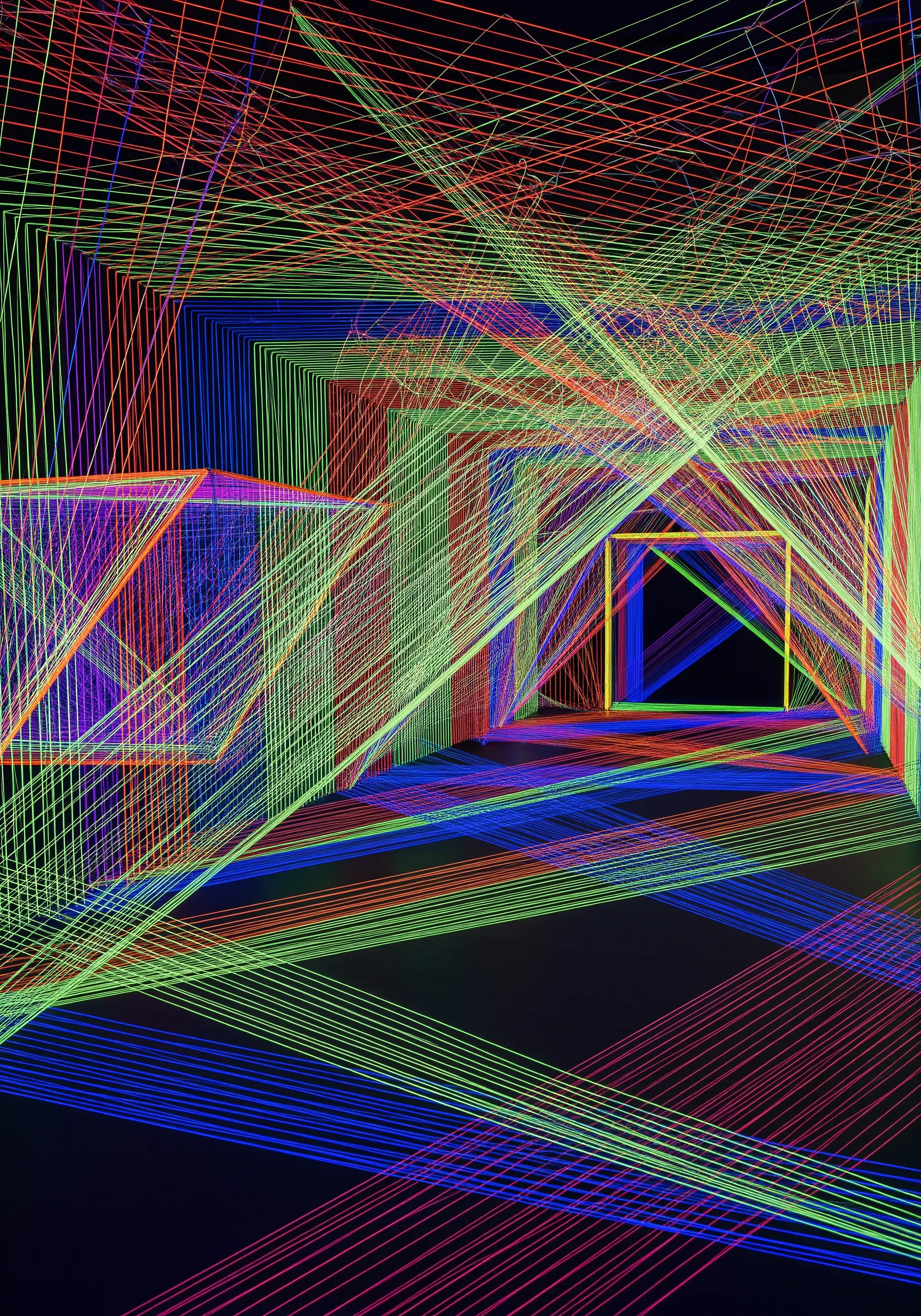An immersive installation of fluorescent red, green, and blue string art creating geometric tunnels.