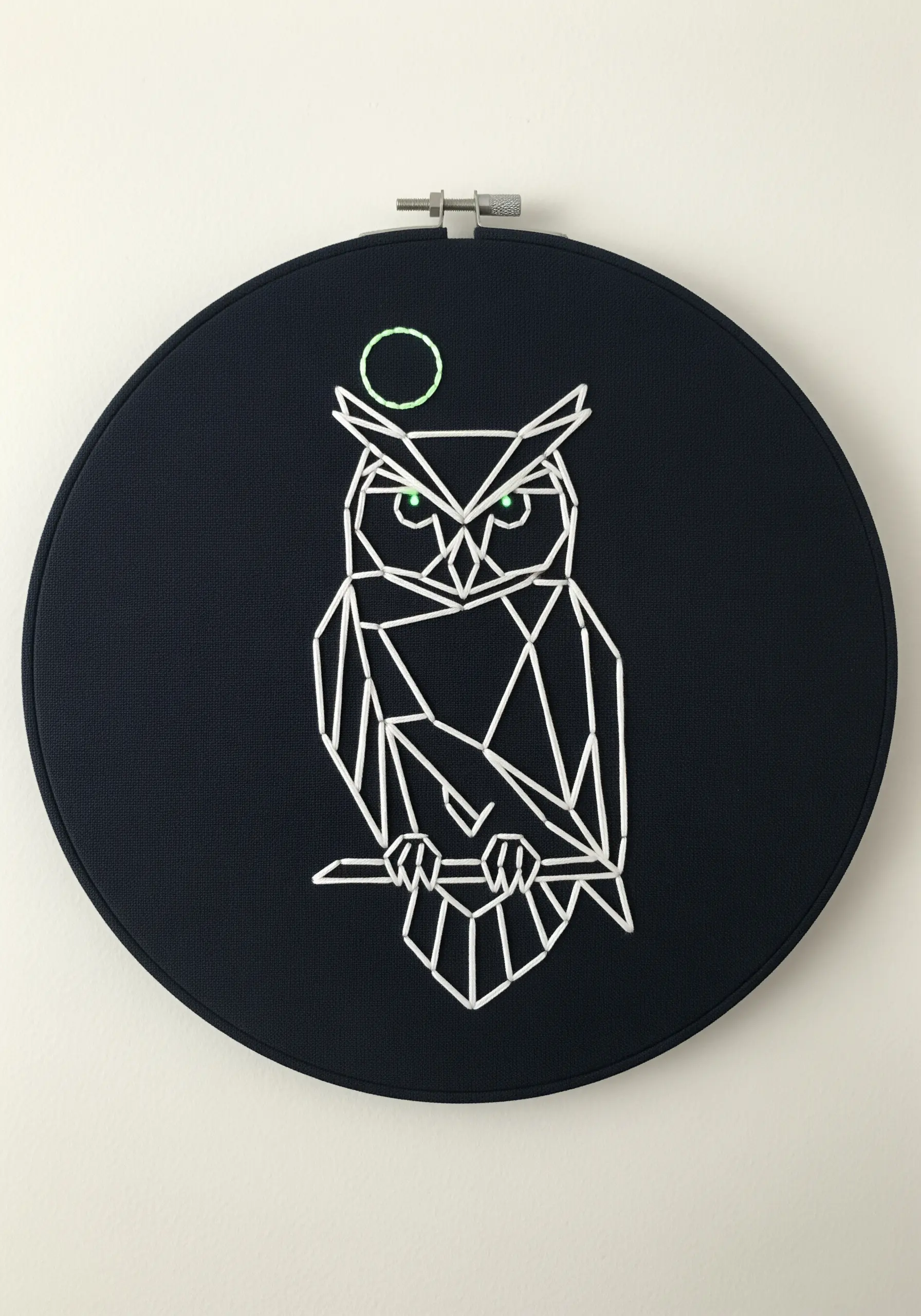 A geometric owl created with thick white lines on dark navy fabric, with minimalist green accents.