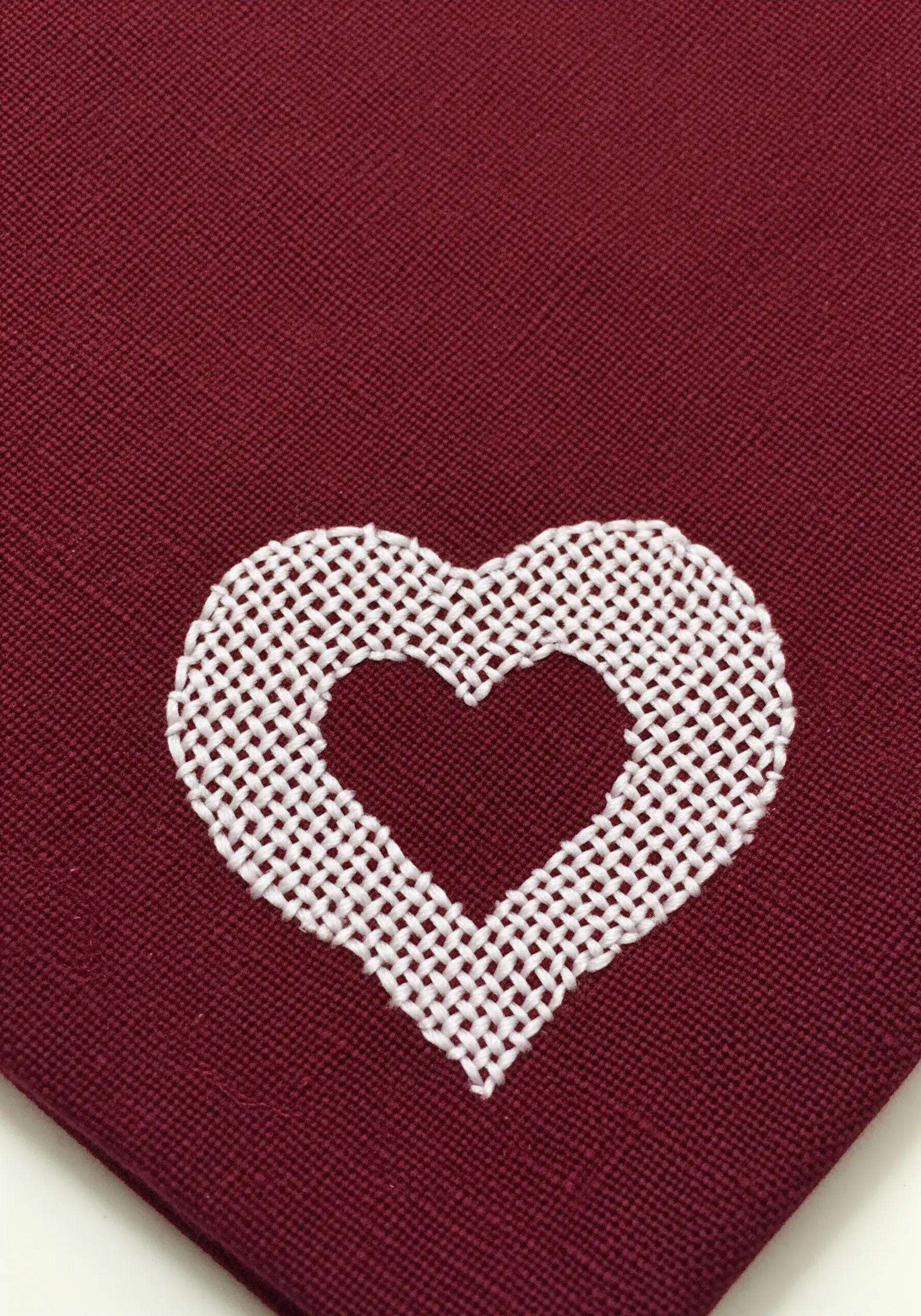 A heart shape created with negative space, outlined by white darning stitches on red fabric.