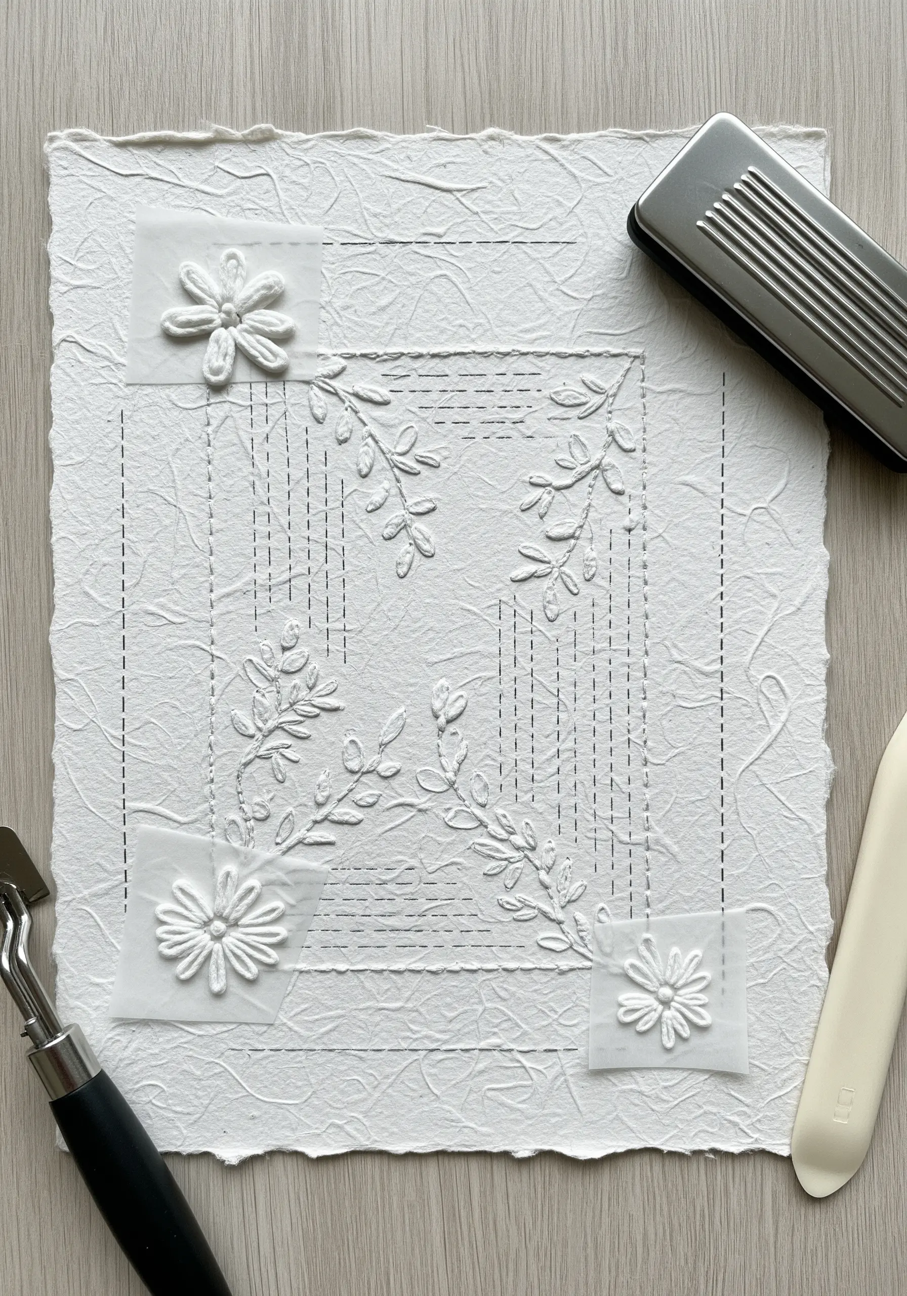 An all-white paper collage featuring embossed floral motifs and dashed-line borders on textured paper.