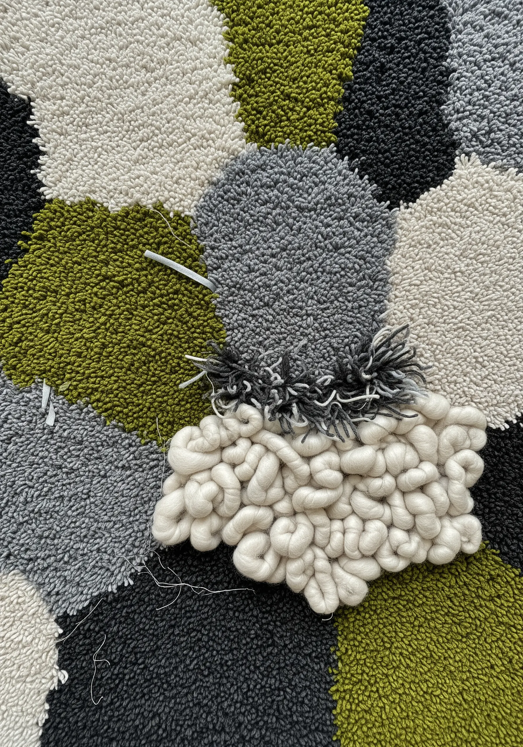 A close-up of a tufted textile piece showing different textures: loops, shag, and chunky wool roving.