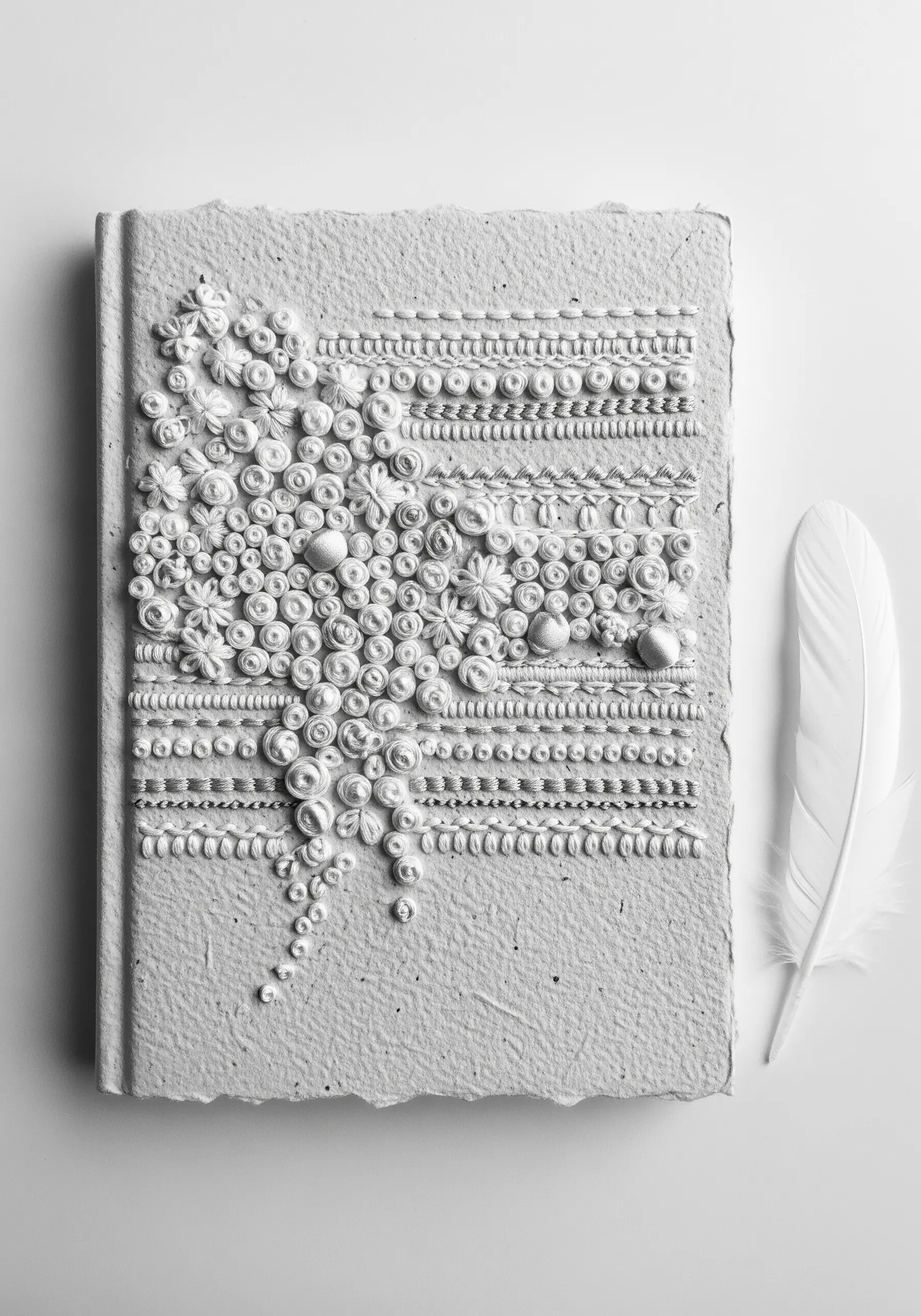 An all-white, highly textural embroidery with knots and raised stitches on a handmade paper journal.