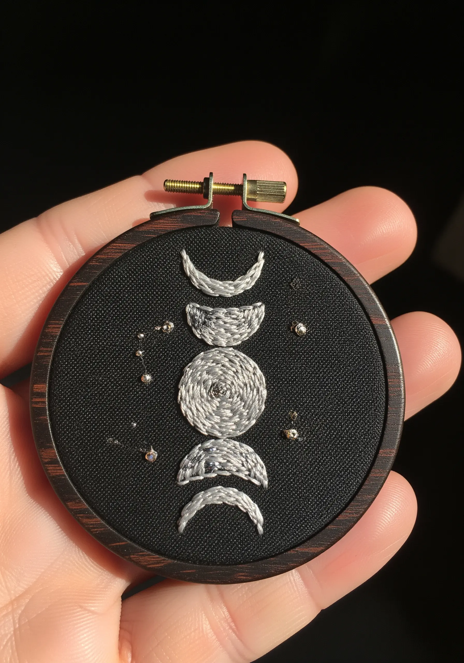 Embroidered moon phases with textured outlines and metallic bead stars on black fabric.
